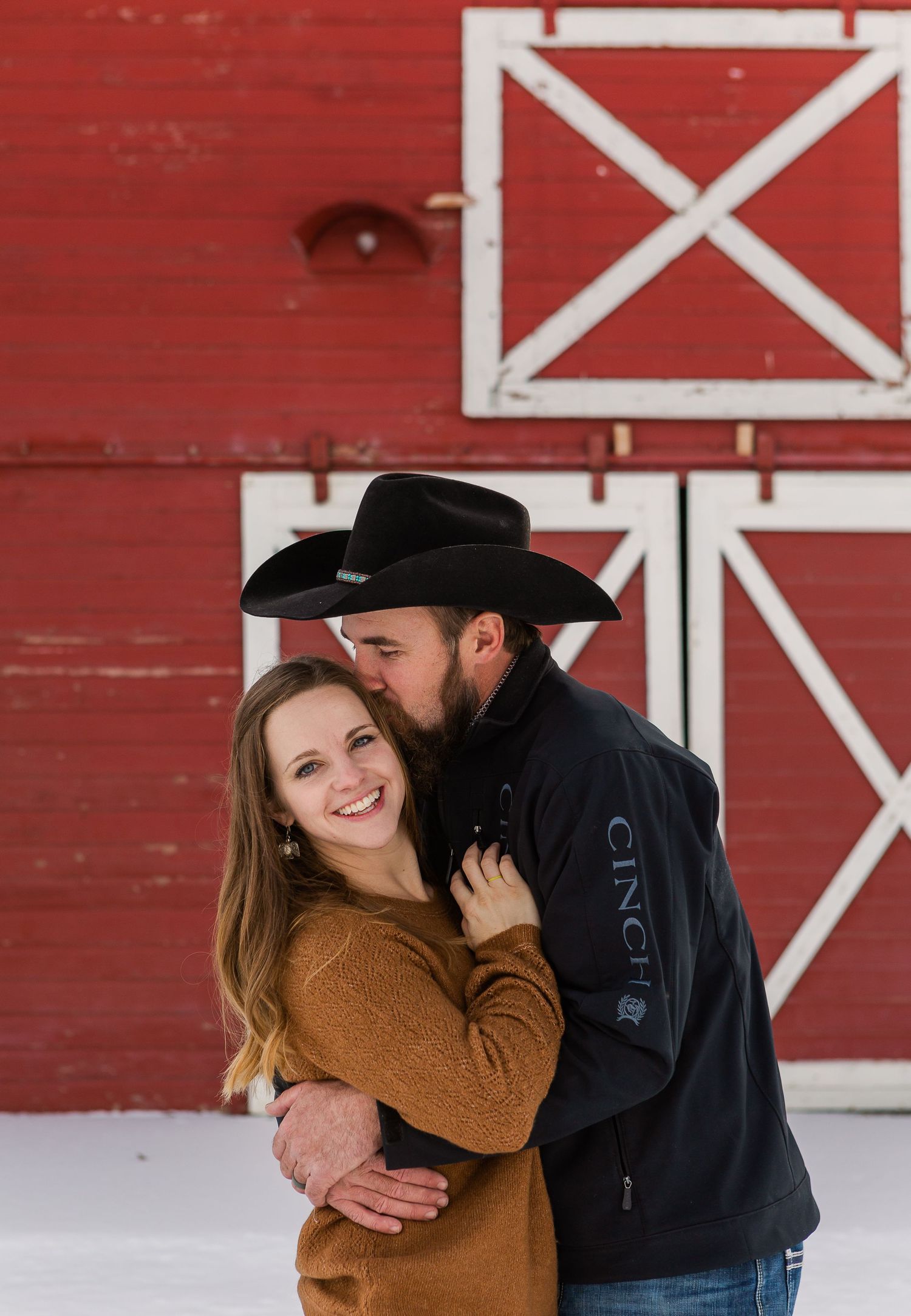 A sweet moment shared between a couple against a bright red barn with white X-pattern doors.