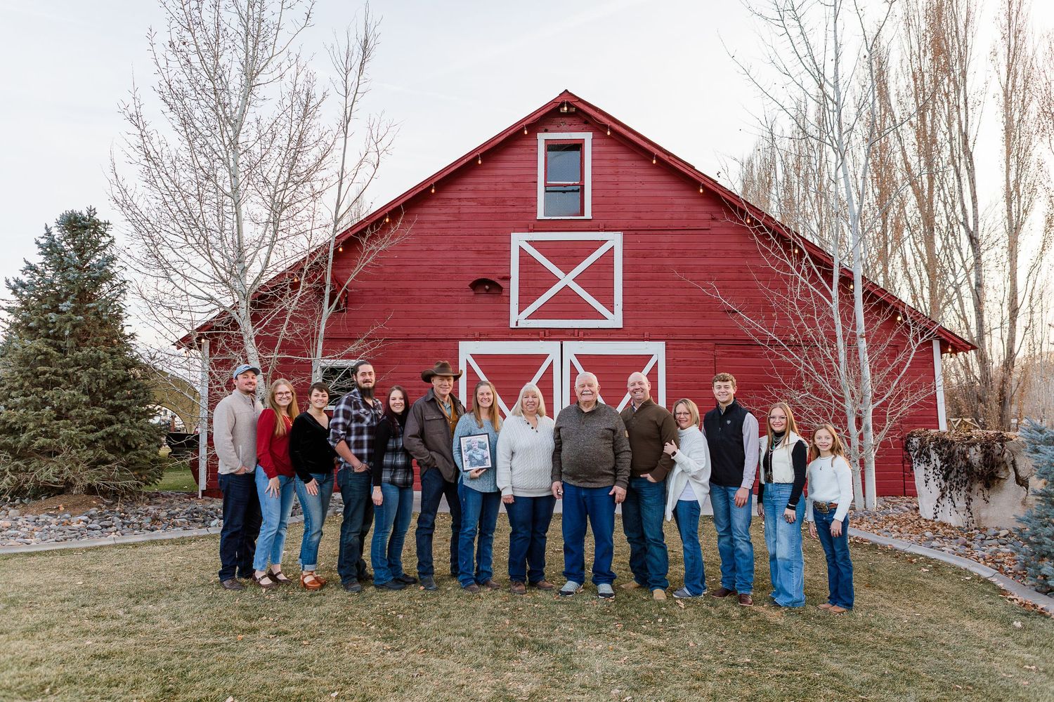 A group of people in casual wear posing together in front of a vibrant red barn with white trim decorations.