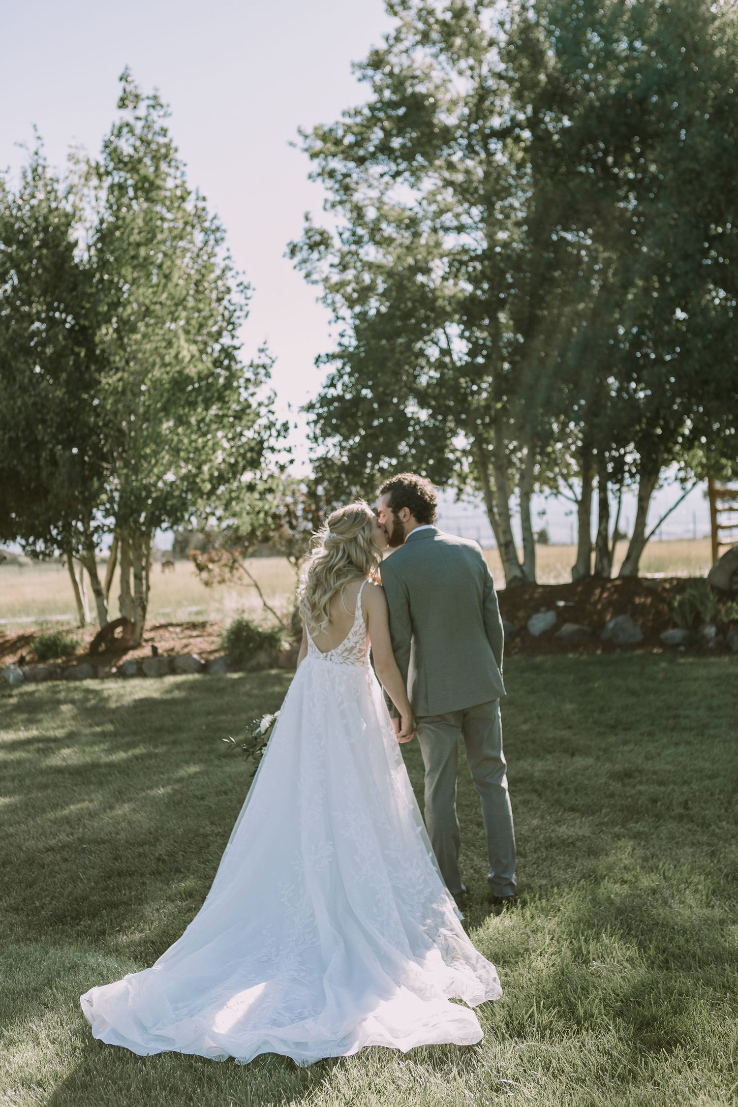 Couple walking away showing bride's elegant train on white wedding dress against natural backdrop.