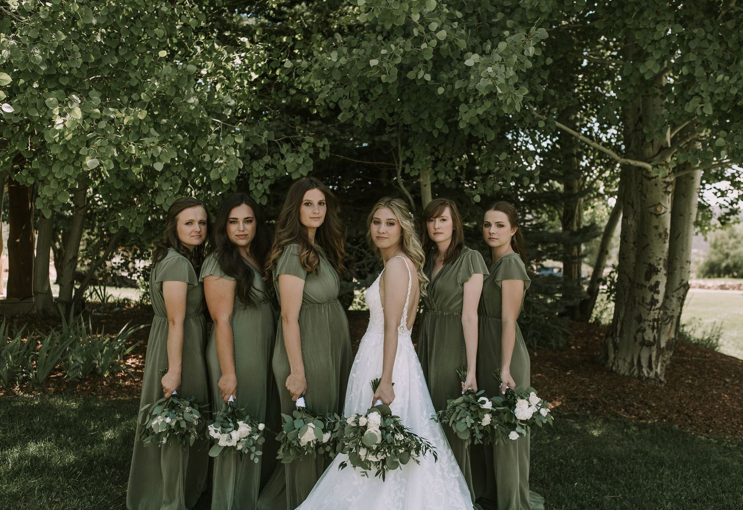 Wedding party portrait with bride in white surrounded by bridesmaids in sage green dresses.
