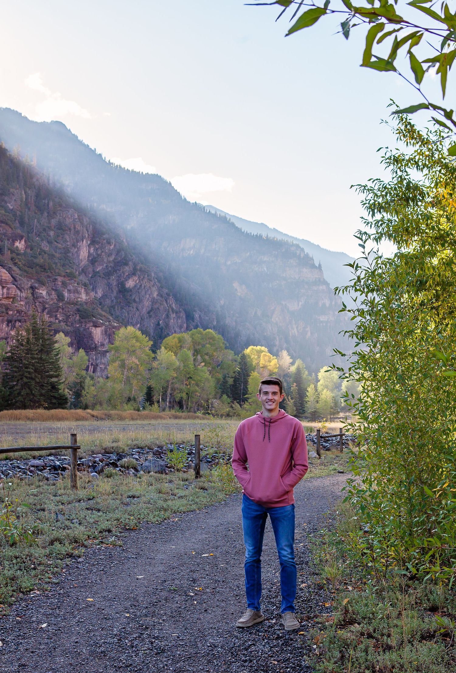 A person in a pink sweatshirt stands on a mountain trail during sunset.