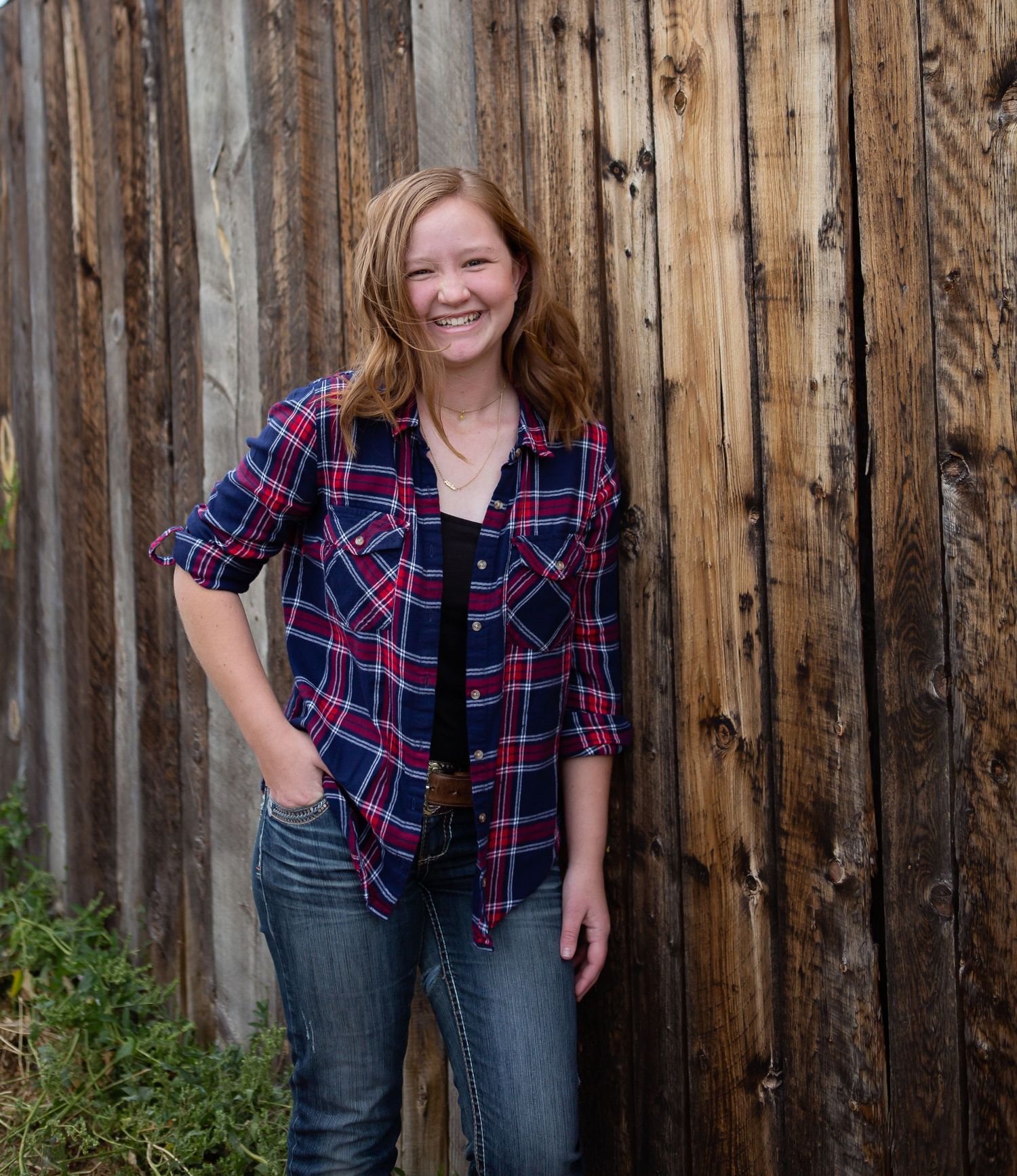 Person in plaid shirt and jeans poses against rustic wooden fence.