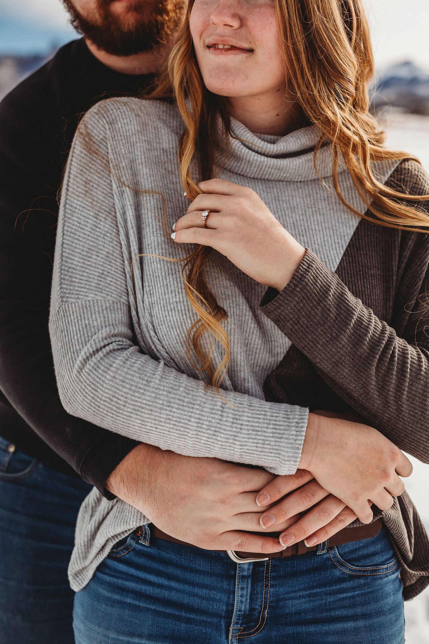 Close-up of a couple embracing, showing off an engagement ring while wearing winter sweaters.