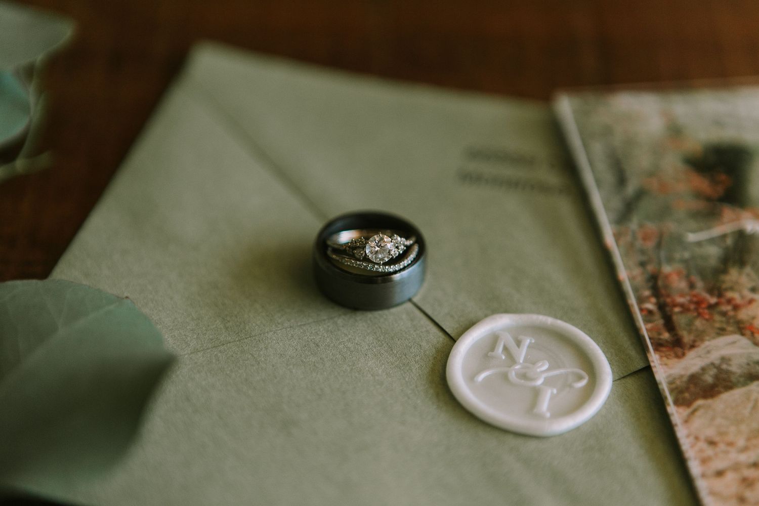 A wedding ring and wax seal on a sage green envelope creating an elegant flat lay.