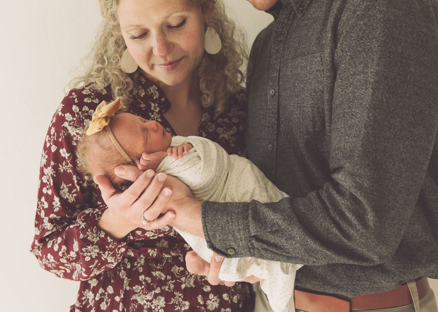 A couple in casual attire tenderly holds their swaddled newborn baby.