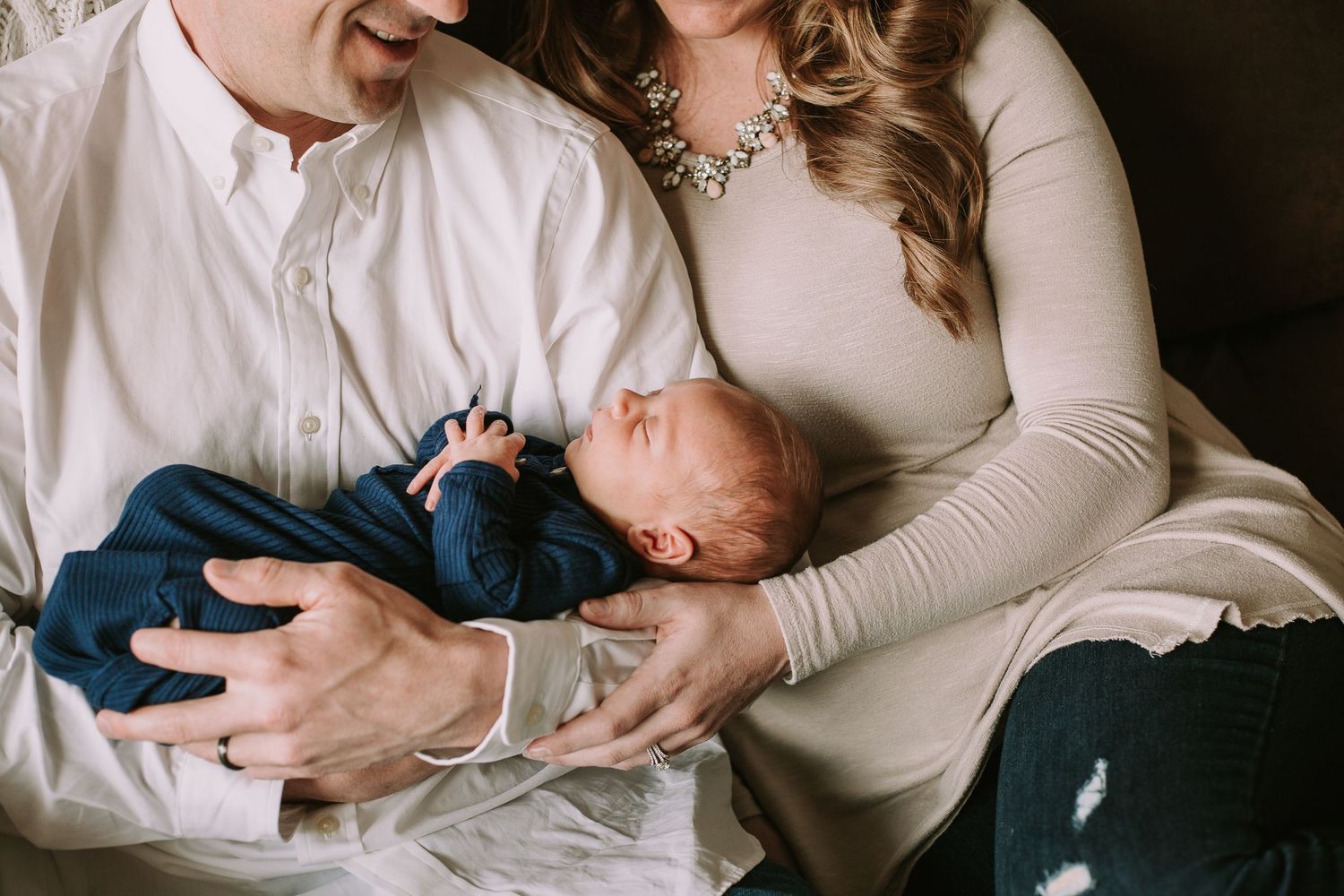 A couple in white and cream clothing share an intimate moment with their newborn.