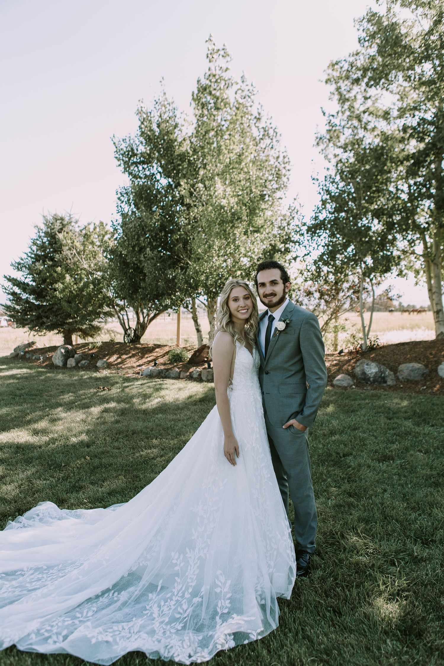 Wedding portrait in garden setting with dramatic lace gown train and sage green suit.