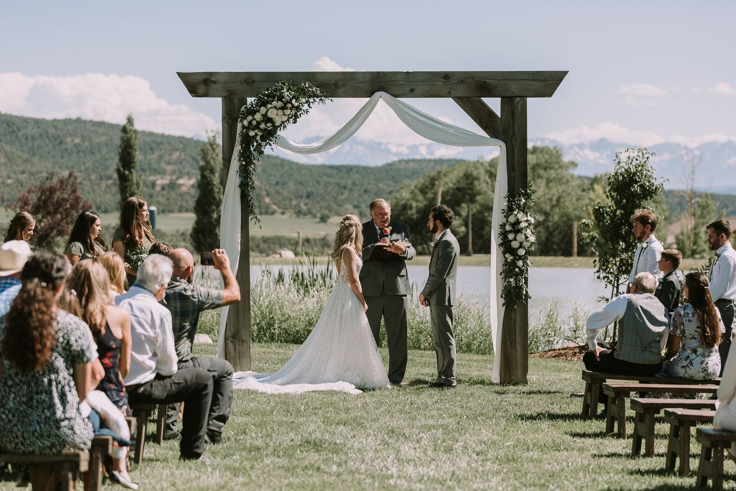 Rustic outdoor wedding ceremony with wooden arch and mountain views.