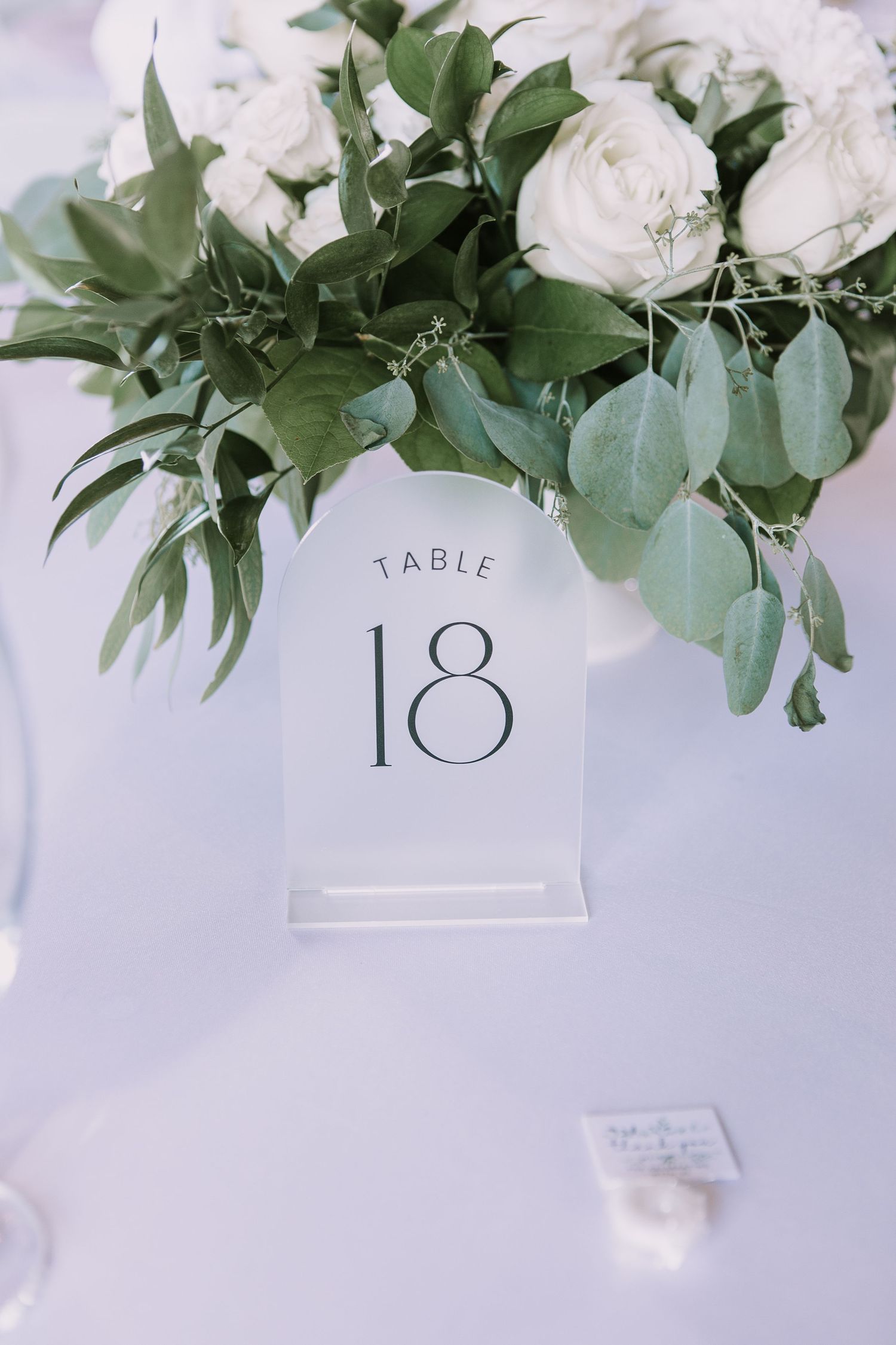 Close-up of table number 18 display with white roses and eucalyptus leaves arrangement.