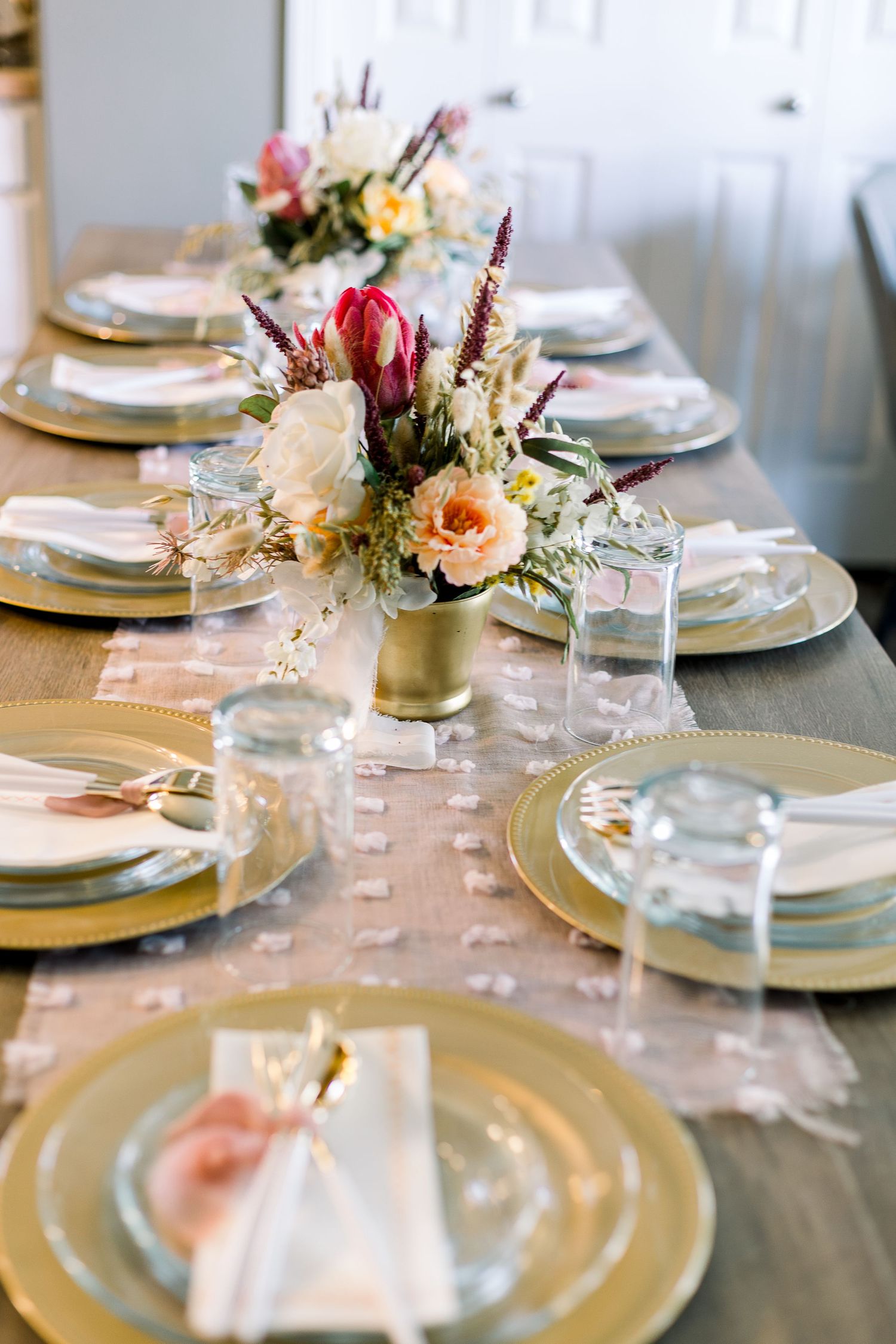 An elegant table setting with gold chargers, pink flowers, and crystal glassware for a formal dinner.