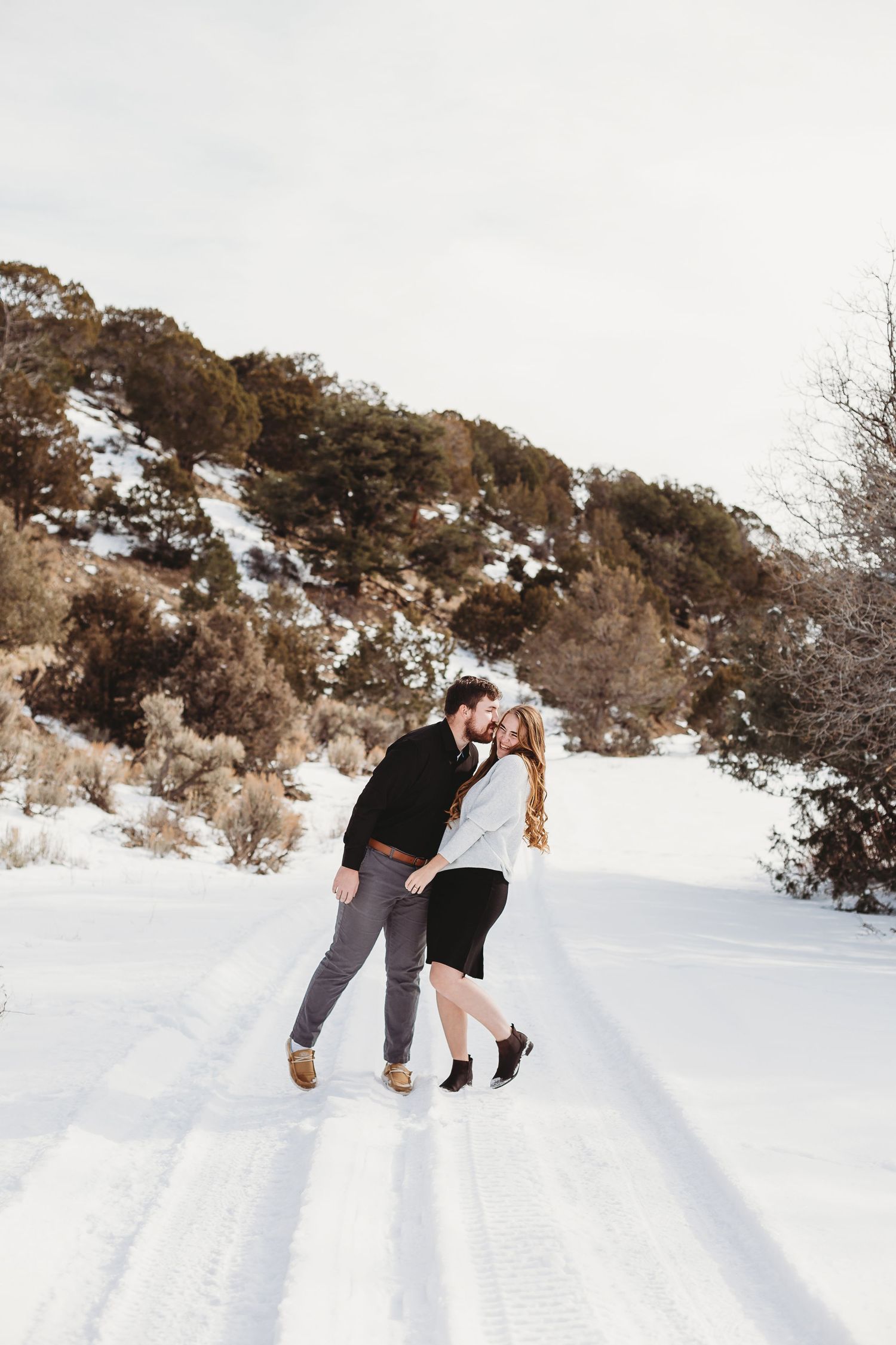 Playful couple dancing together on a snowy mountain trail.