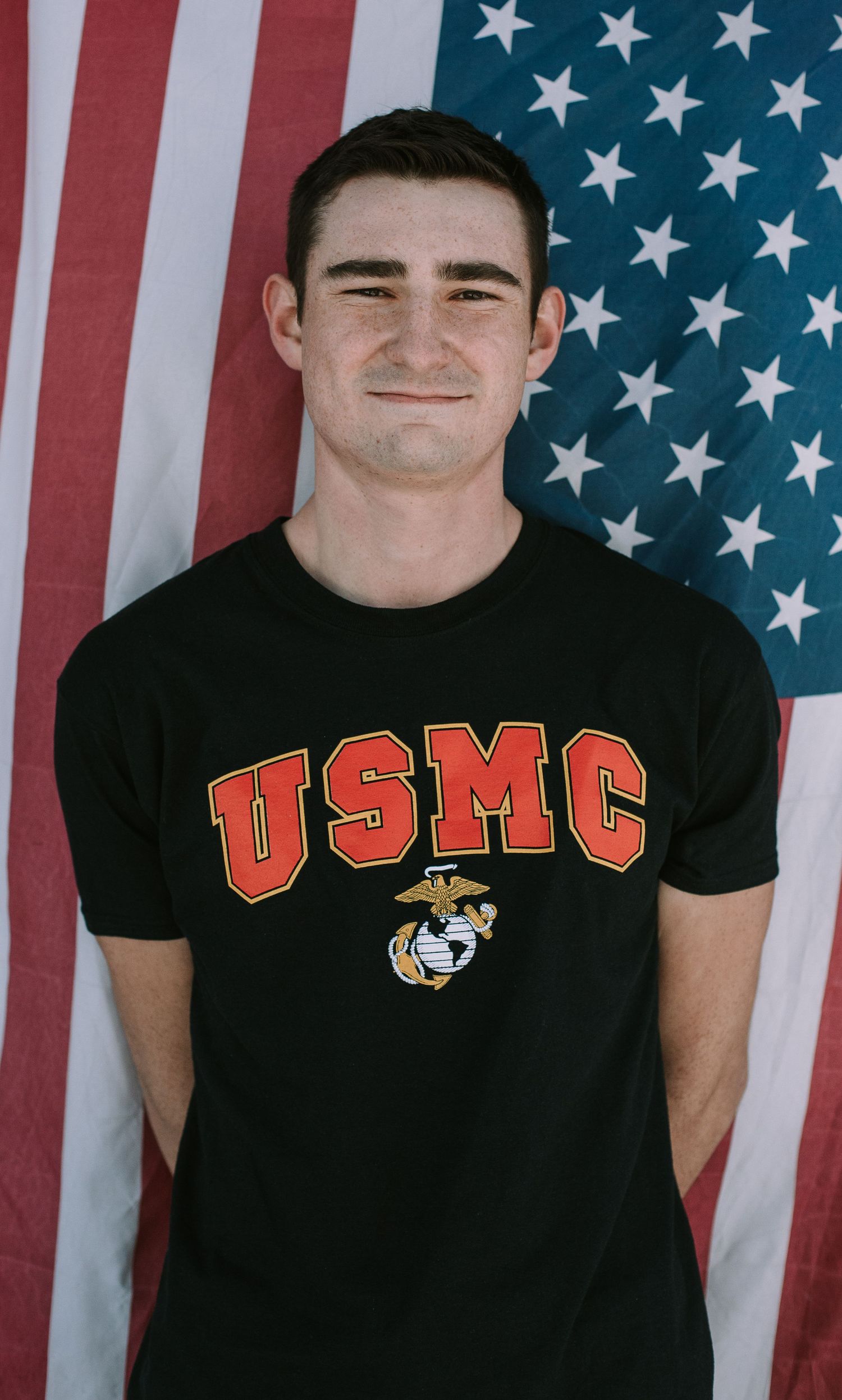 Person in USMC t-shirt poses against American flag background.