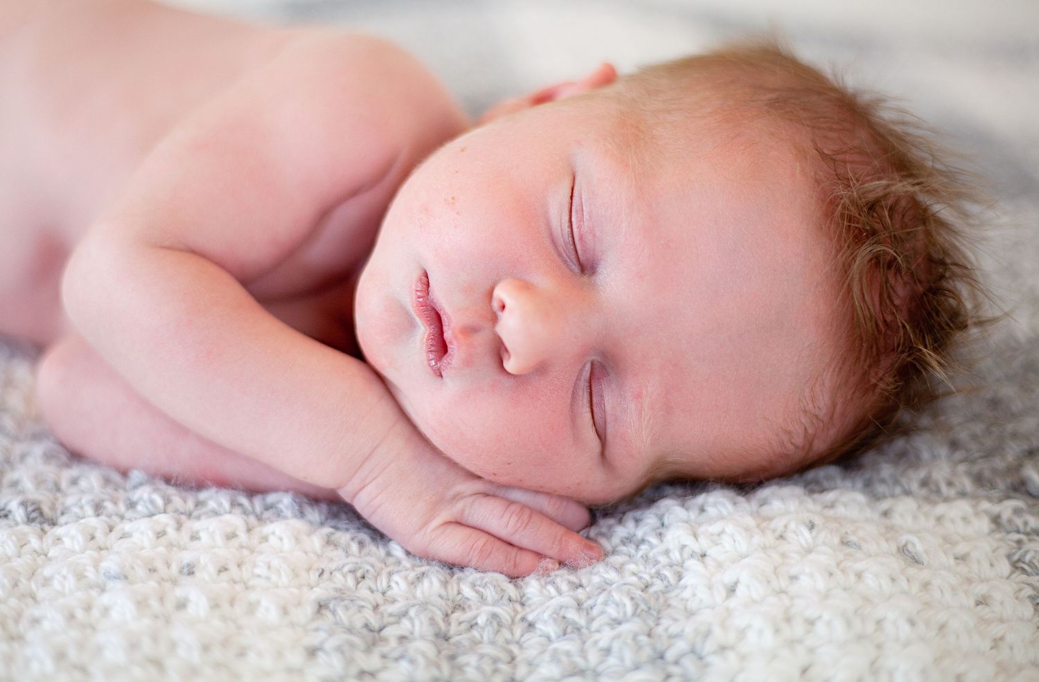 Peaceful sleeping newborn with rosy skin resting on textured white blanket.