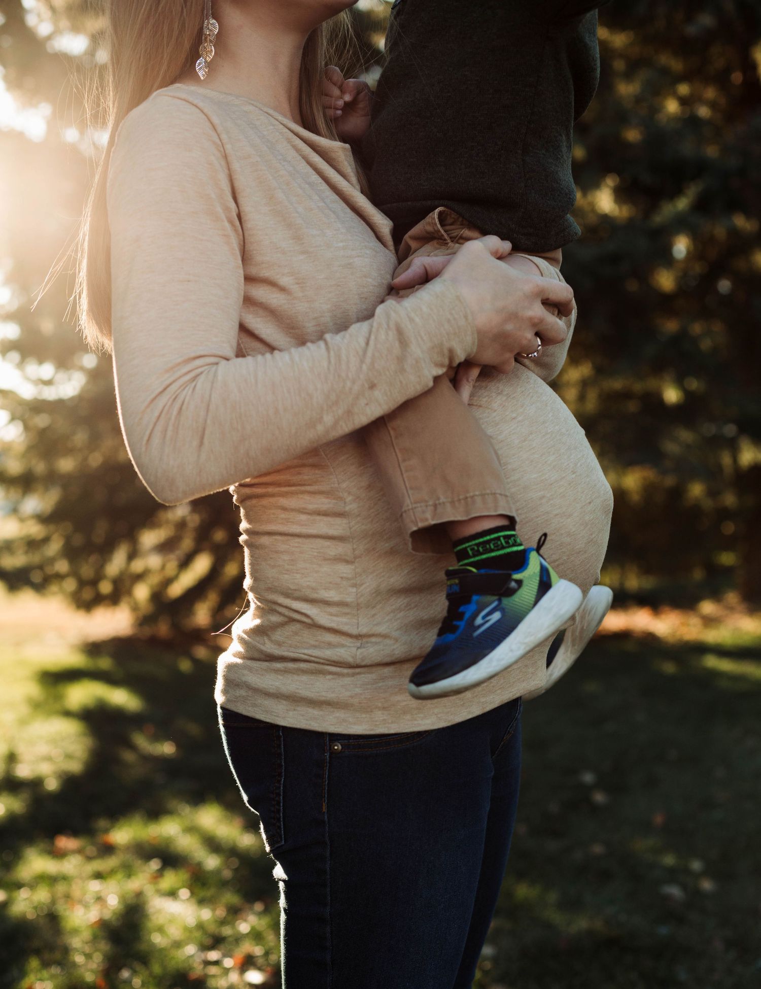 Close-up of pregnant woman's belly with small child's feet visible in casual outdoor setting.