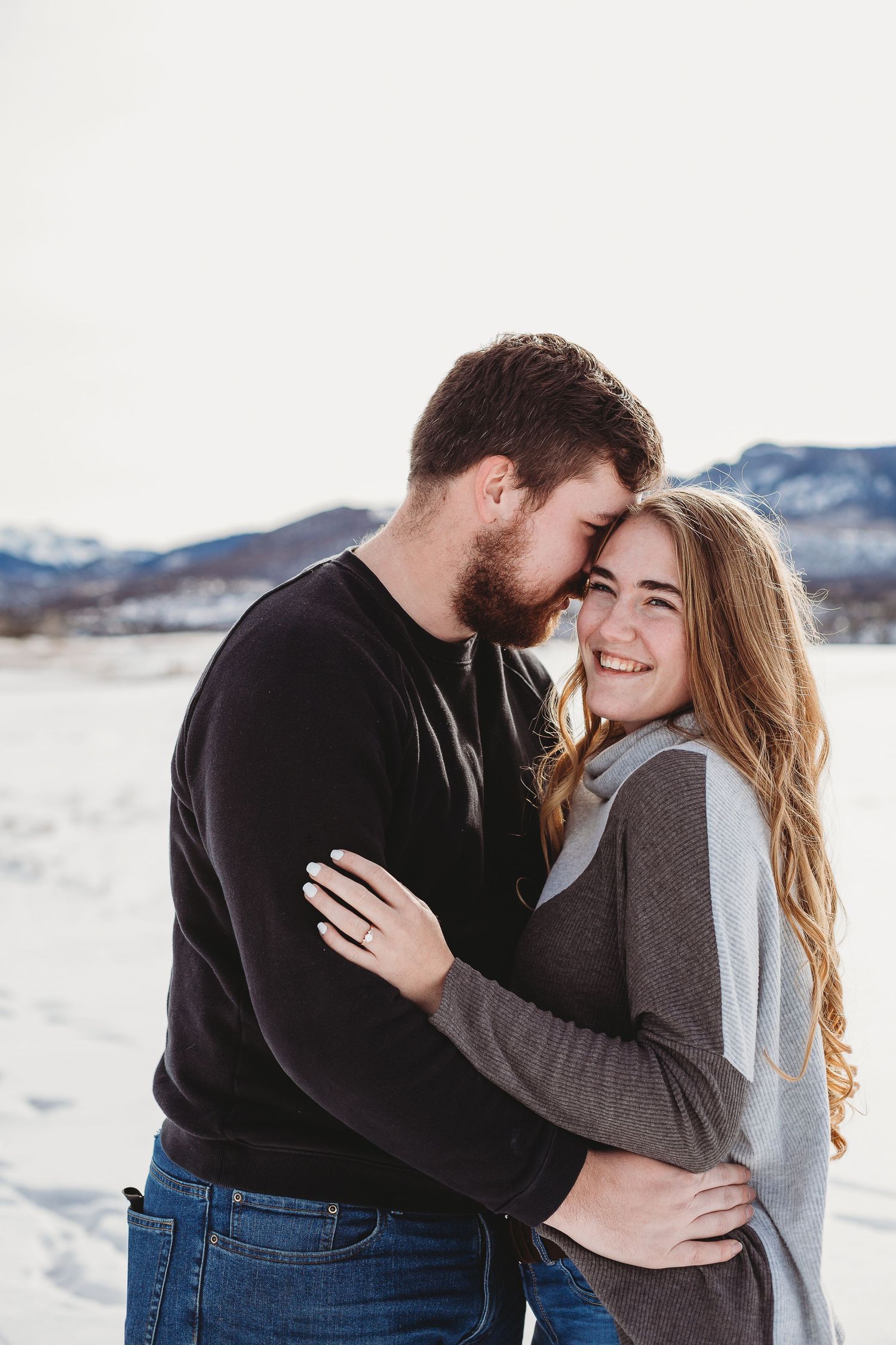 A joyful couple embraces and laughs together in front of snow-covered mountains.