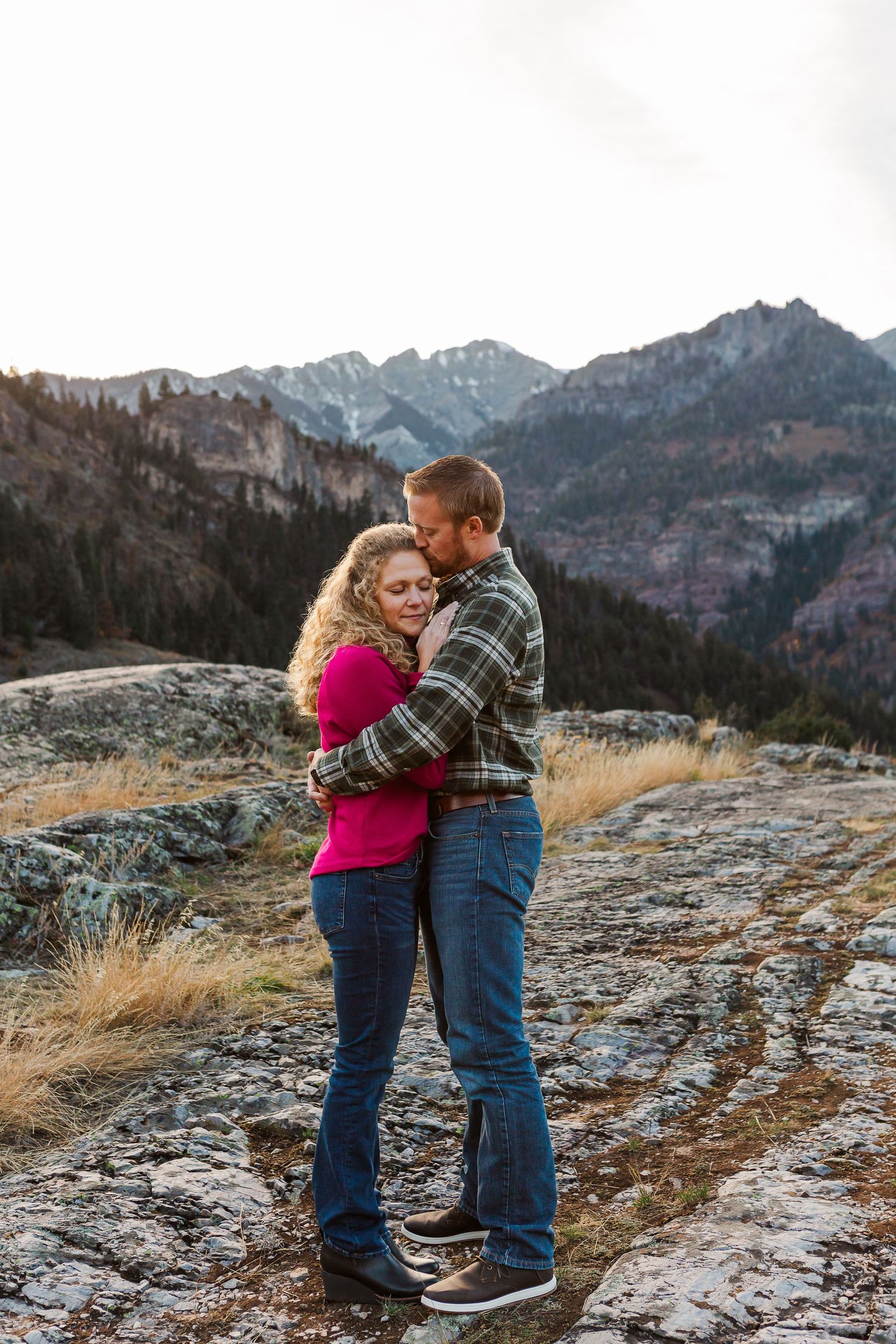A romantic embrace captured on a mountain overlook with dramatic peaks and dry grass in the background.