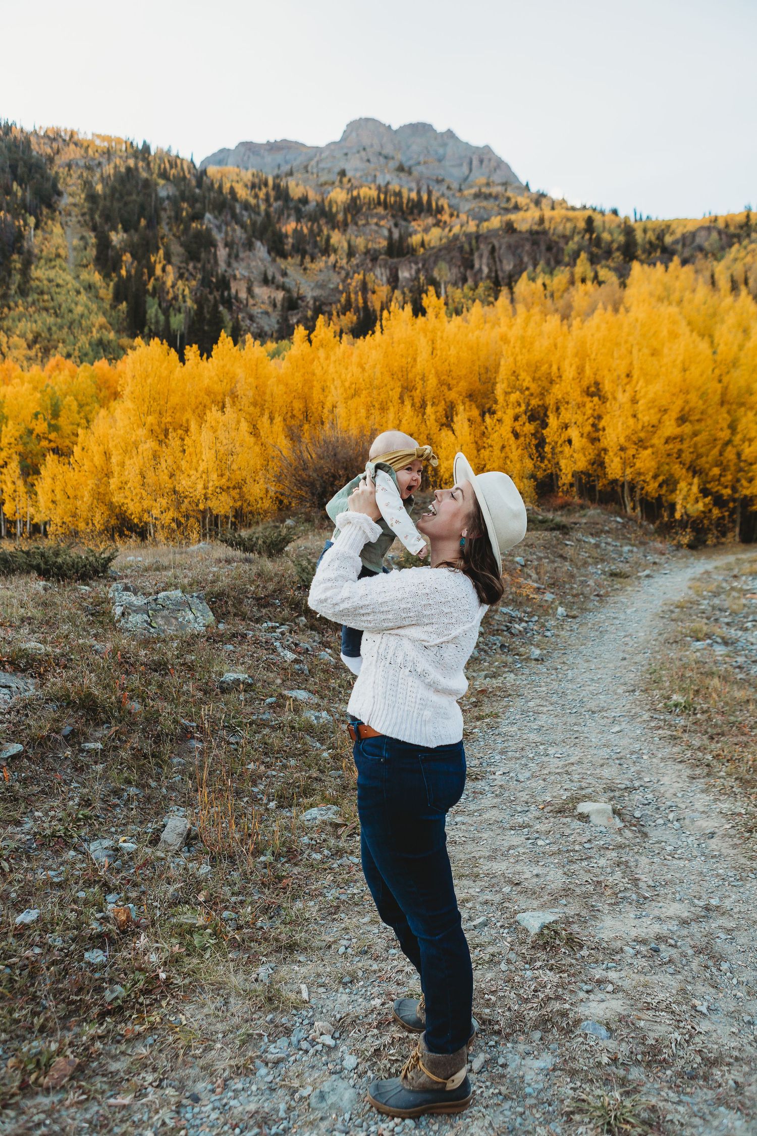 Fall hiker on mountain trail admires vibrant yellow aspen trees against rocky cliffs in autumn landscape.