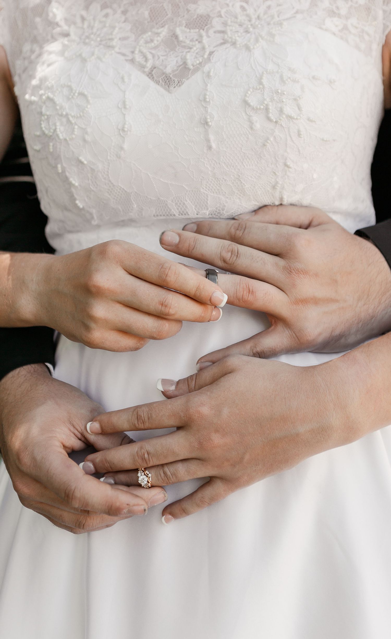 Closeup of hands wearing wedding rings against a white lace wedding dress.