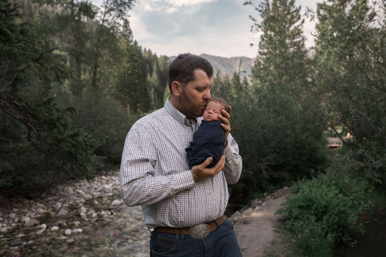 A tender moment between parent and baby on a mountain trail surrounded by pine trees.
