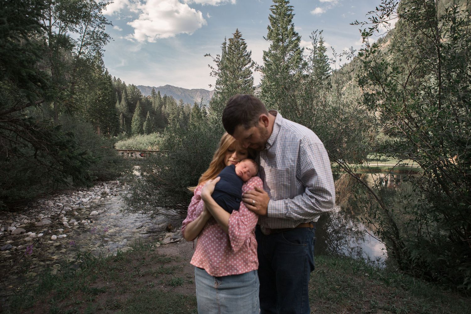 Intimate family scene along mountain creek with evergreen forest in background.
