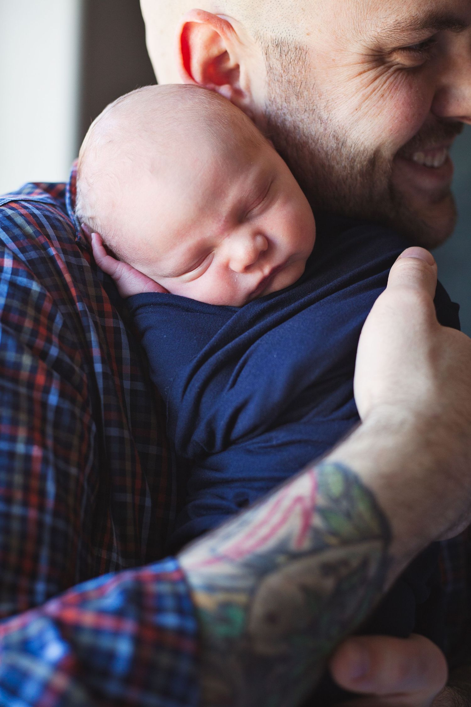 A sleeping baby rests peacefully against a tattooed arm in plaid.