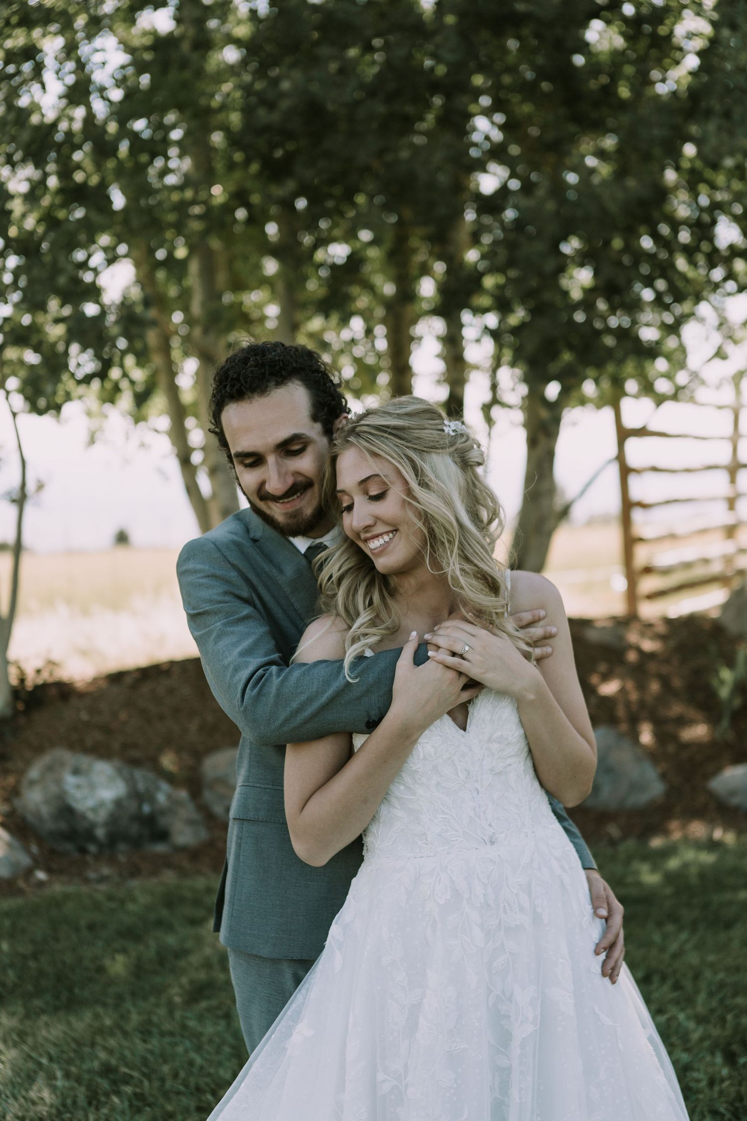 Joyful wedding couple shares tender moment outdoors with natural backdrop.