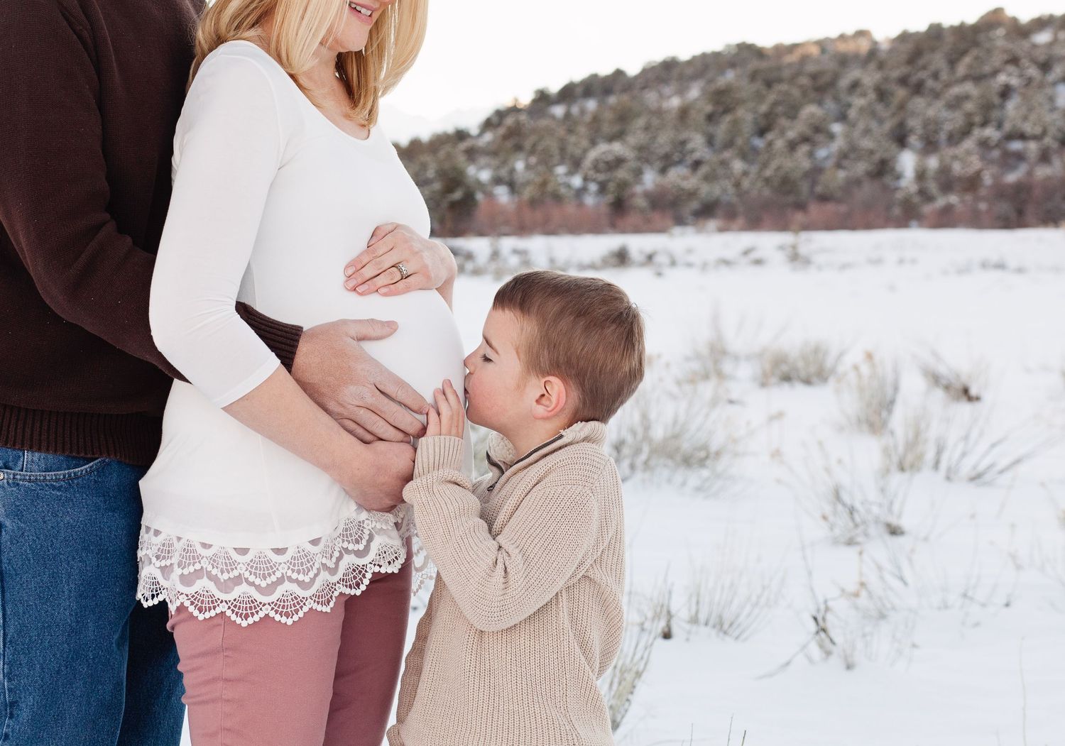 Tender moment between expectant mother and child in winter setting.
