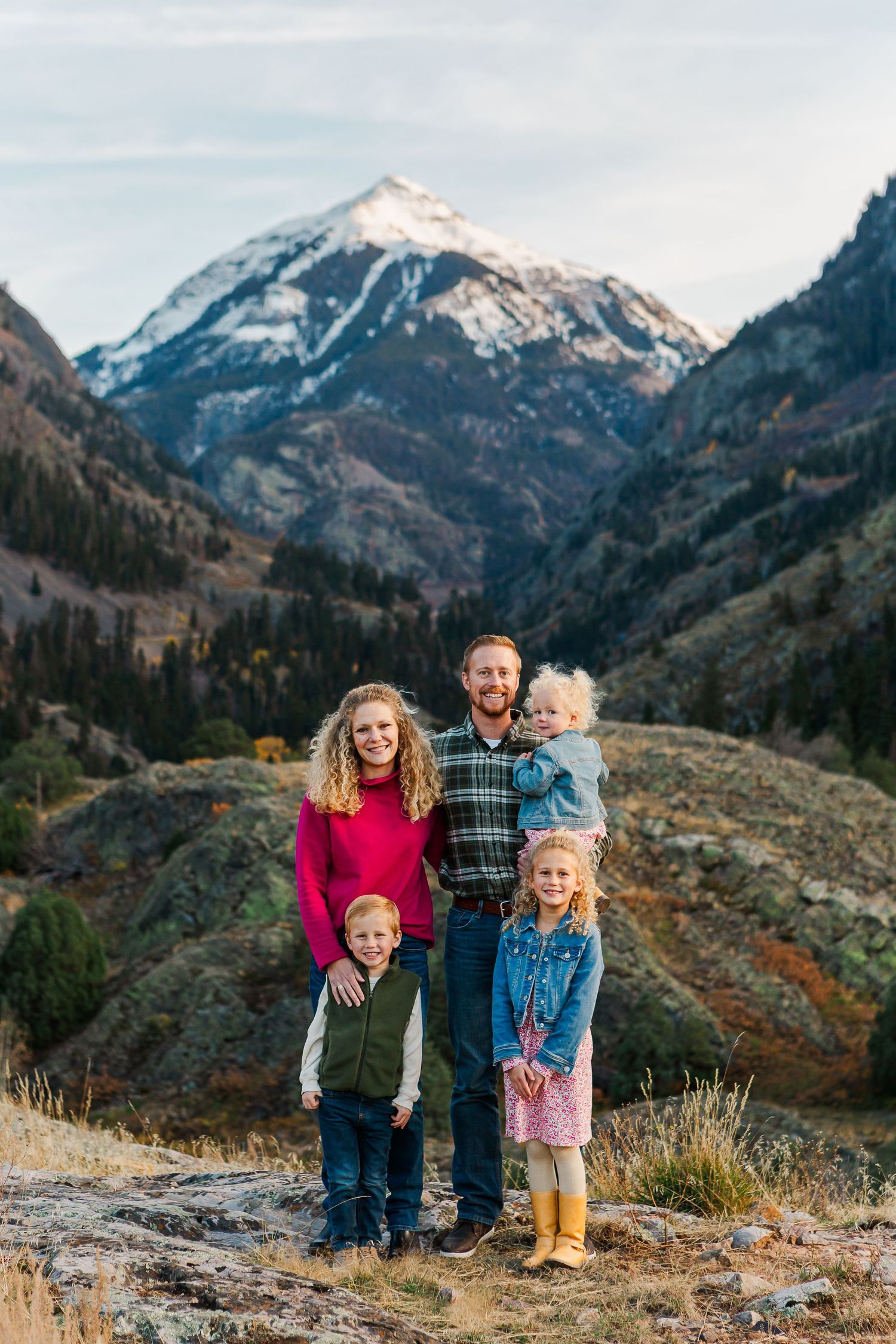 A family of five poses together on a mountain overlook with snow-capped peaks in the background.