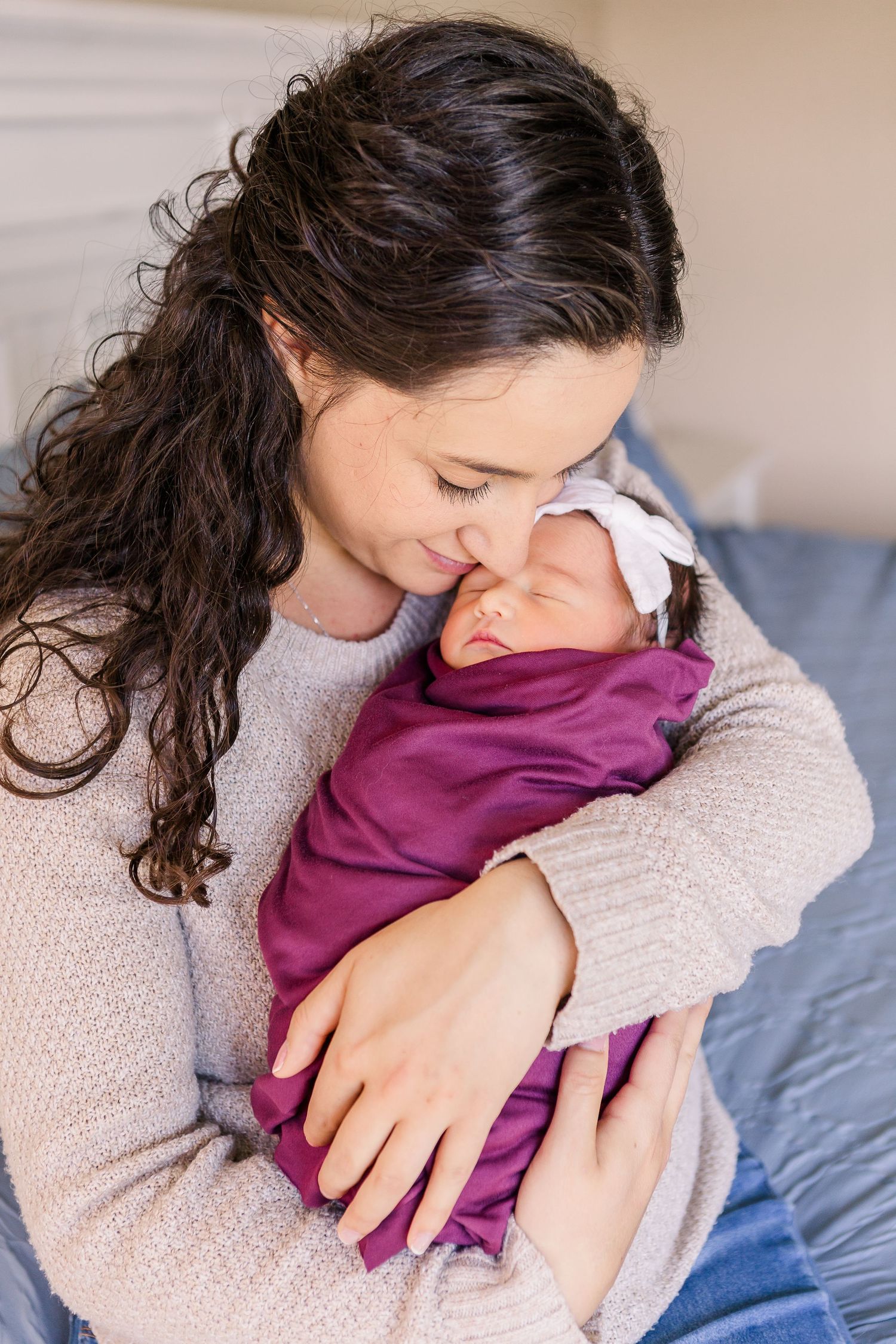 A tender moment between a parent and newborn baby wrapped in purple, sitting on blue bedding.