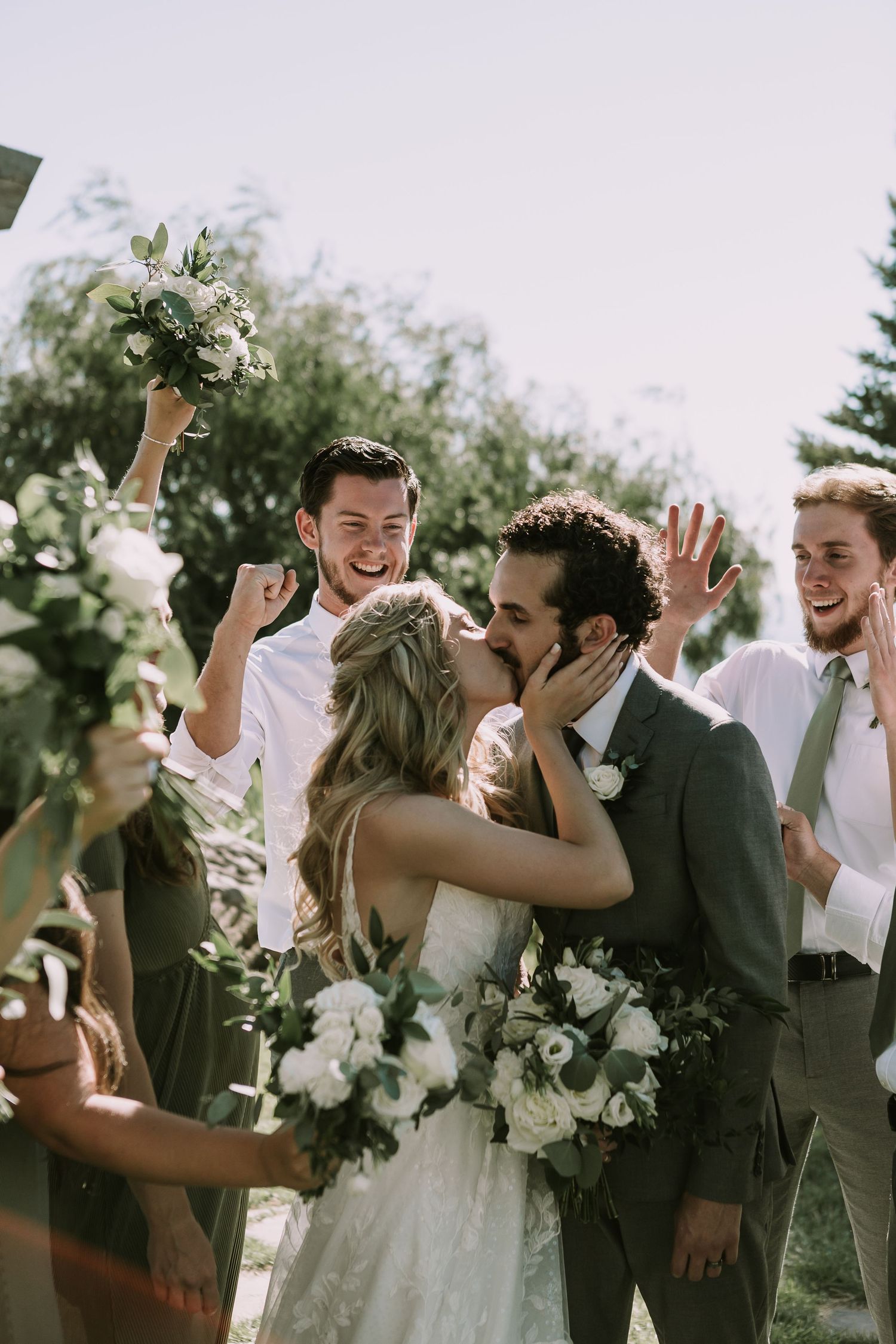 Joyful celebration moment with wedding party cheering under decorated arch.