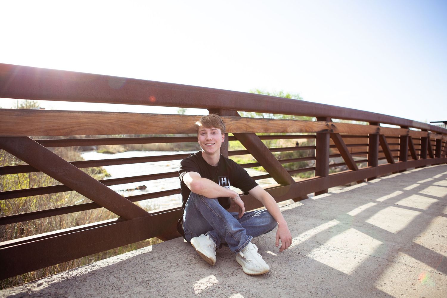 Person sitting casually on metal bridge railing during daytime photo shoot.