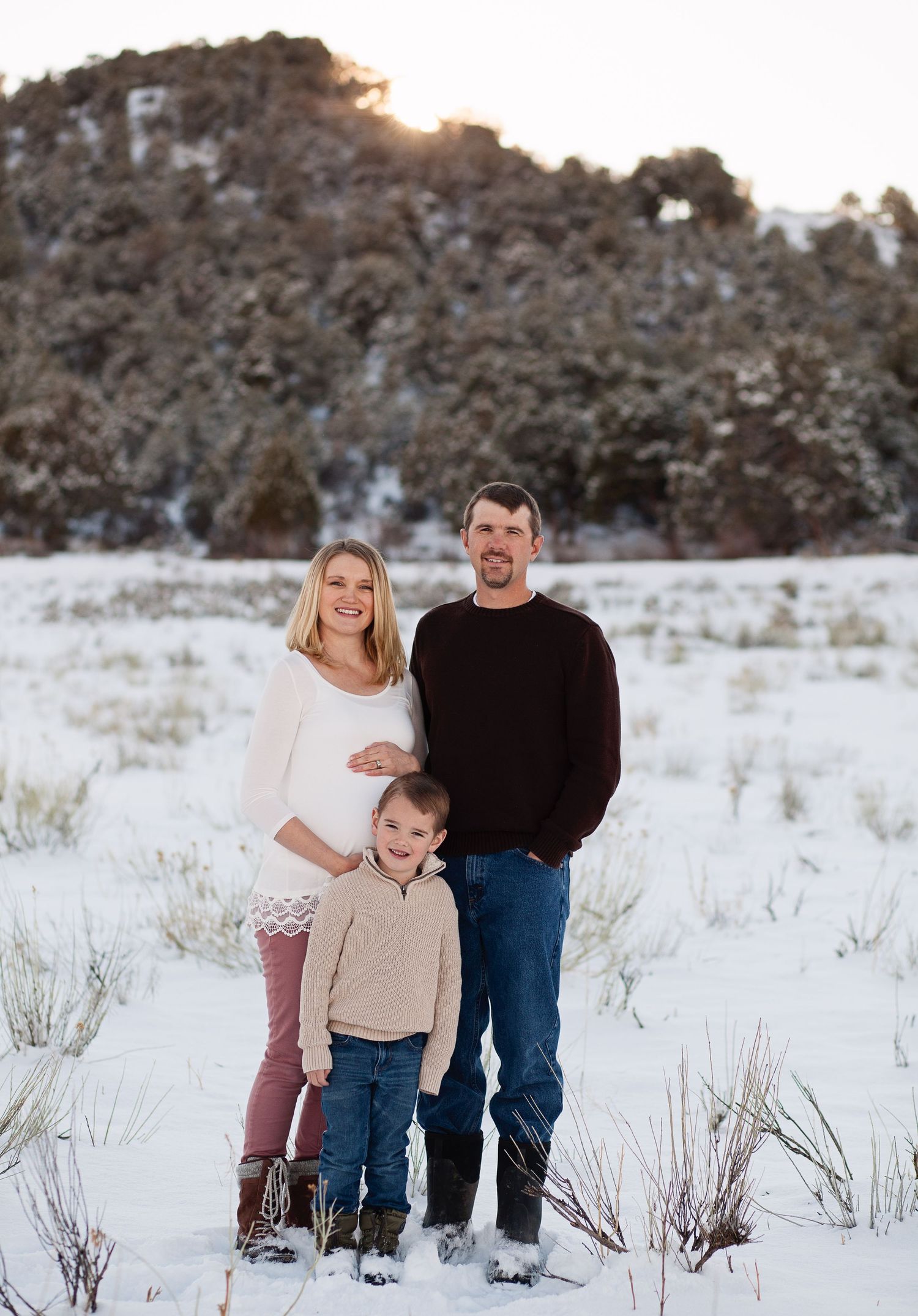 Winter family portrait with snowy mountain backdrop and warm sunset lighting.