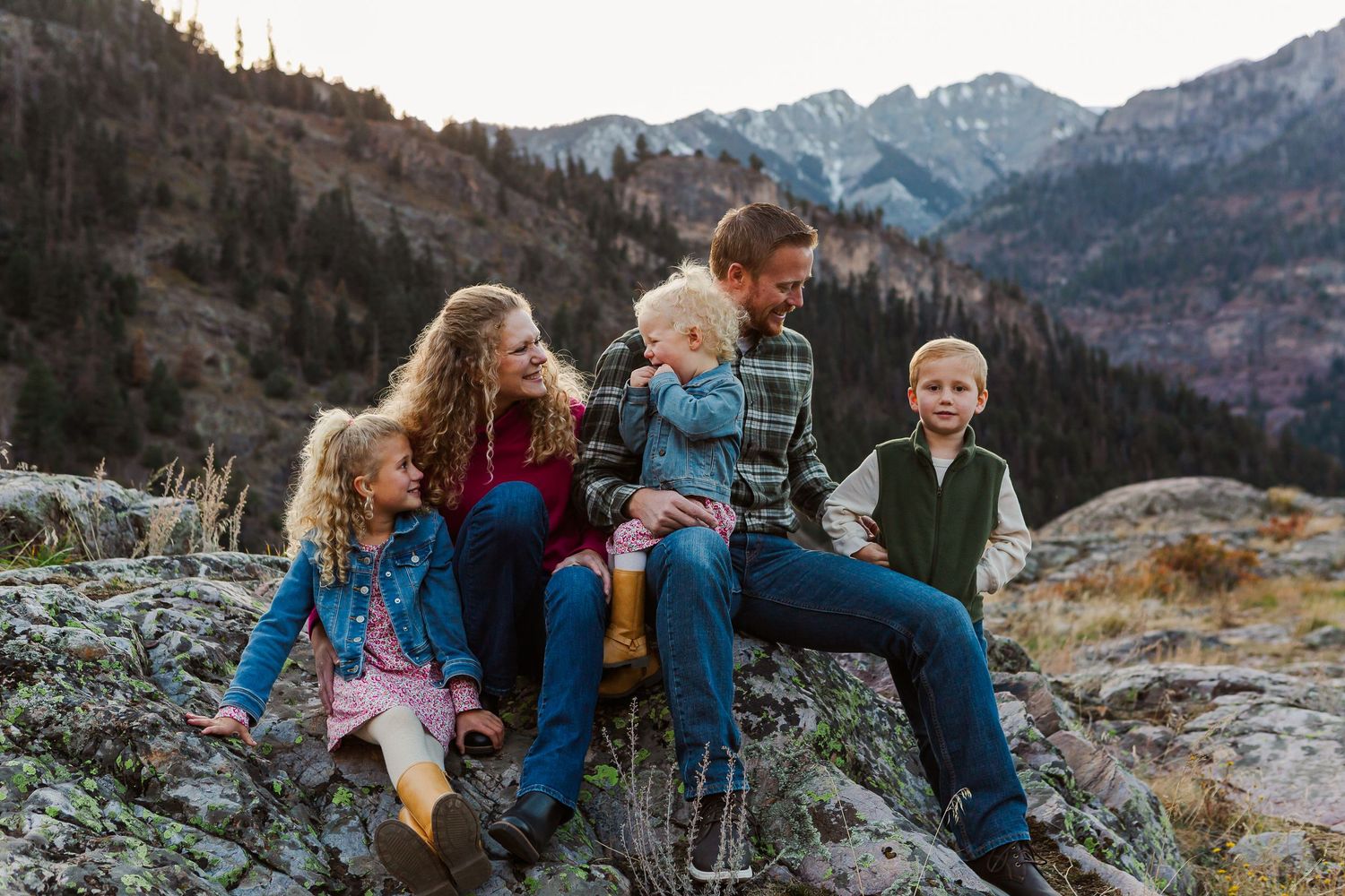 A group sits together on rocky terrain with snow-capped mountains visible in the background.