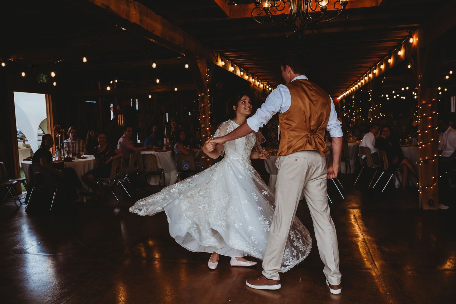 A couple dancing at their wedding reception in a rustic barn venue with string lights.