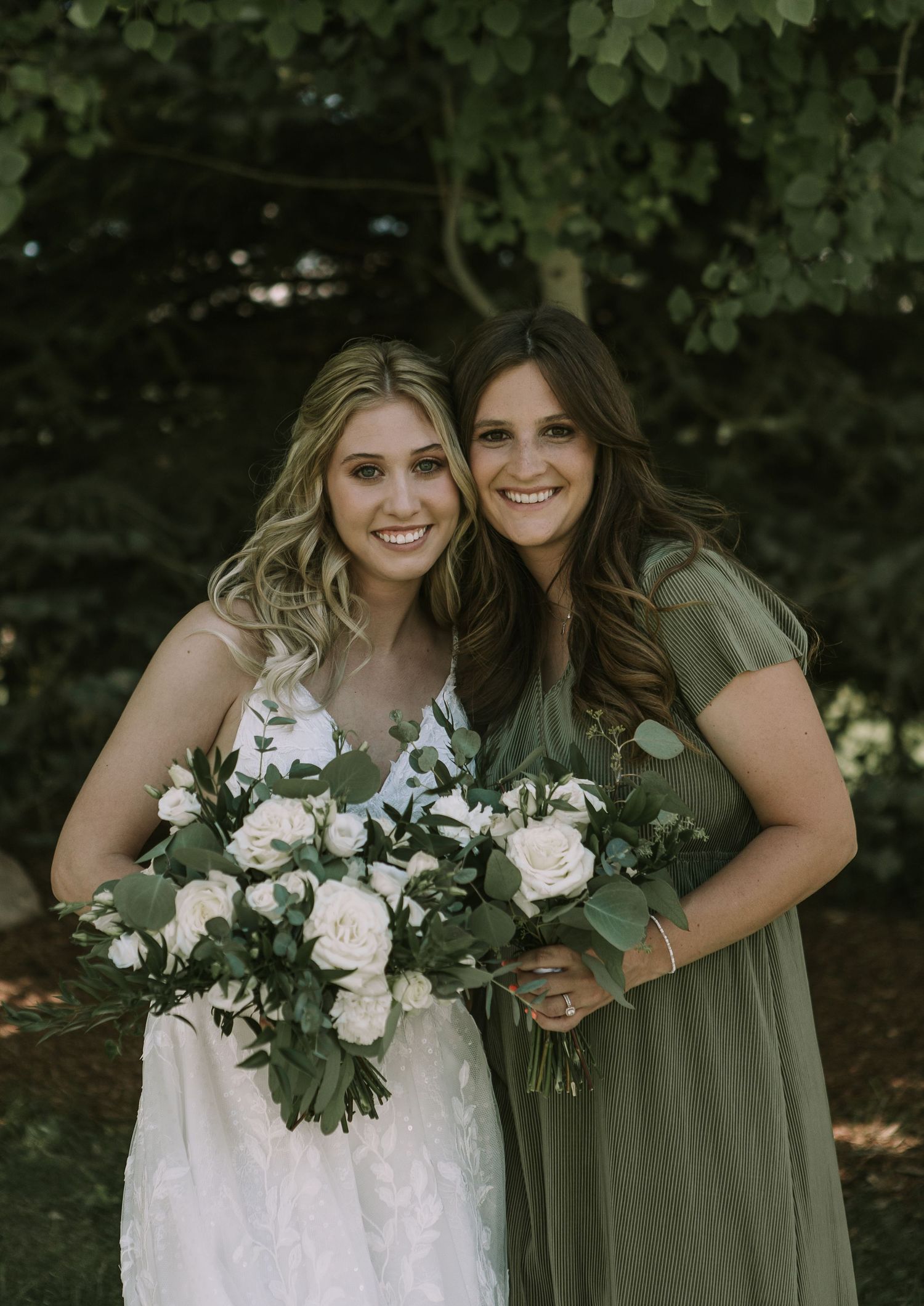 Bride with bridesmaid sharing joyful moment while holding white rose bouquets.