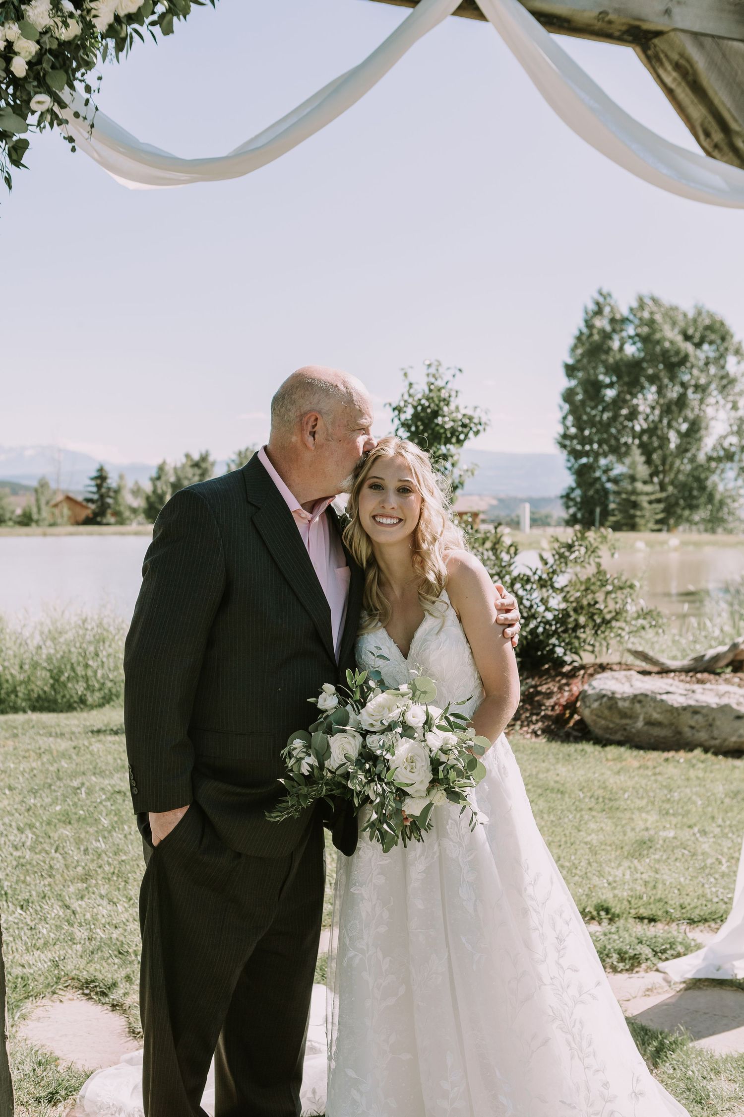 Sweet moment between bride and guest under decorative wedding arch at outdoor ceremony.