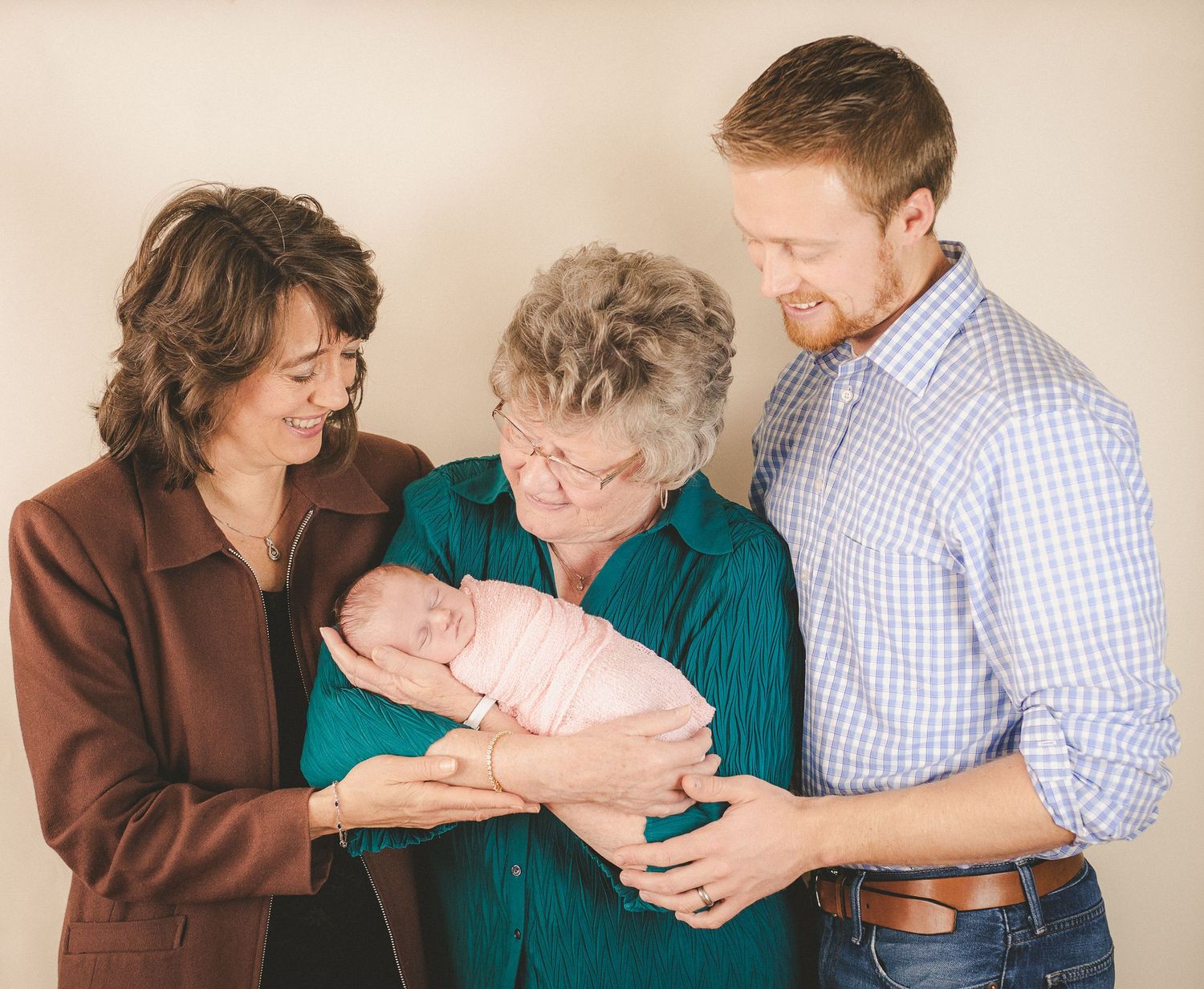 Three generations gather to admire and hold a sleeping newborn baby in a heartwarming portrait.