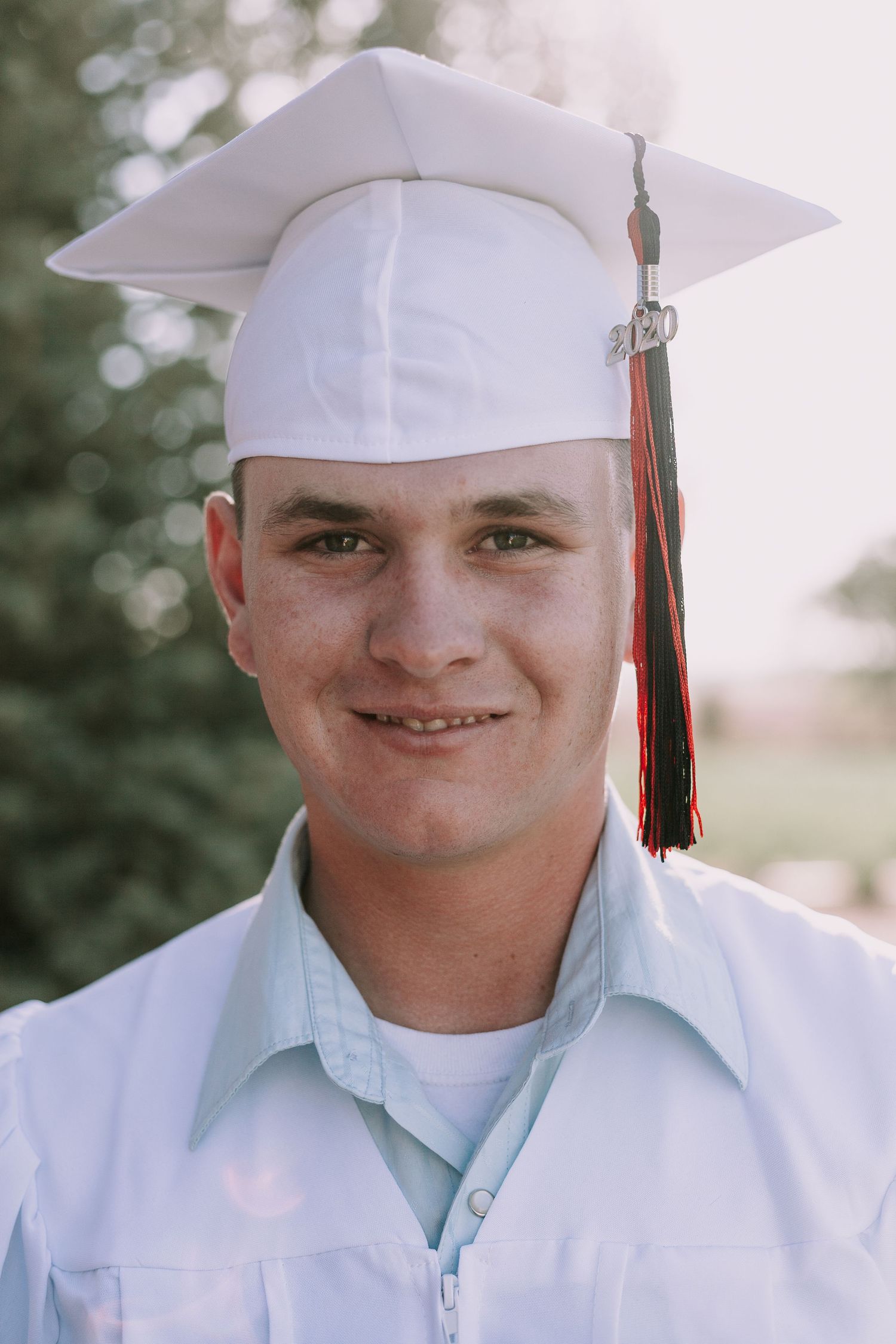 Graduate wearing white cap and gown with tassel and green stole during outdoor graduation photo session.