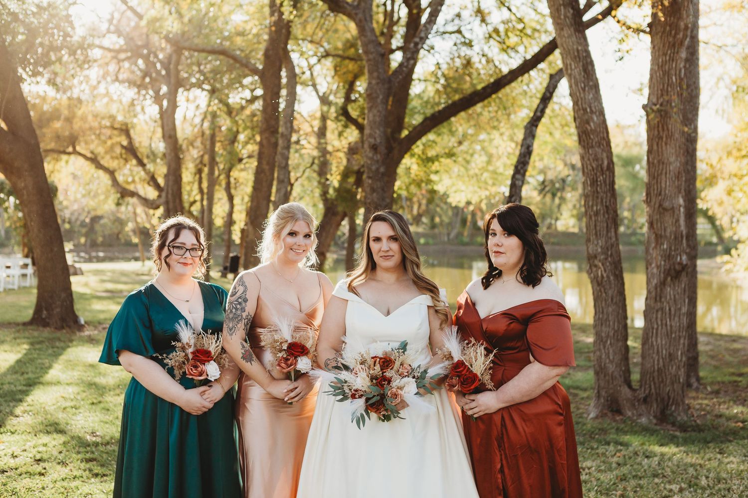 Bridal party in jewel-toned dresses poses together during outdoor autumn wedding.