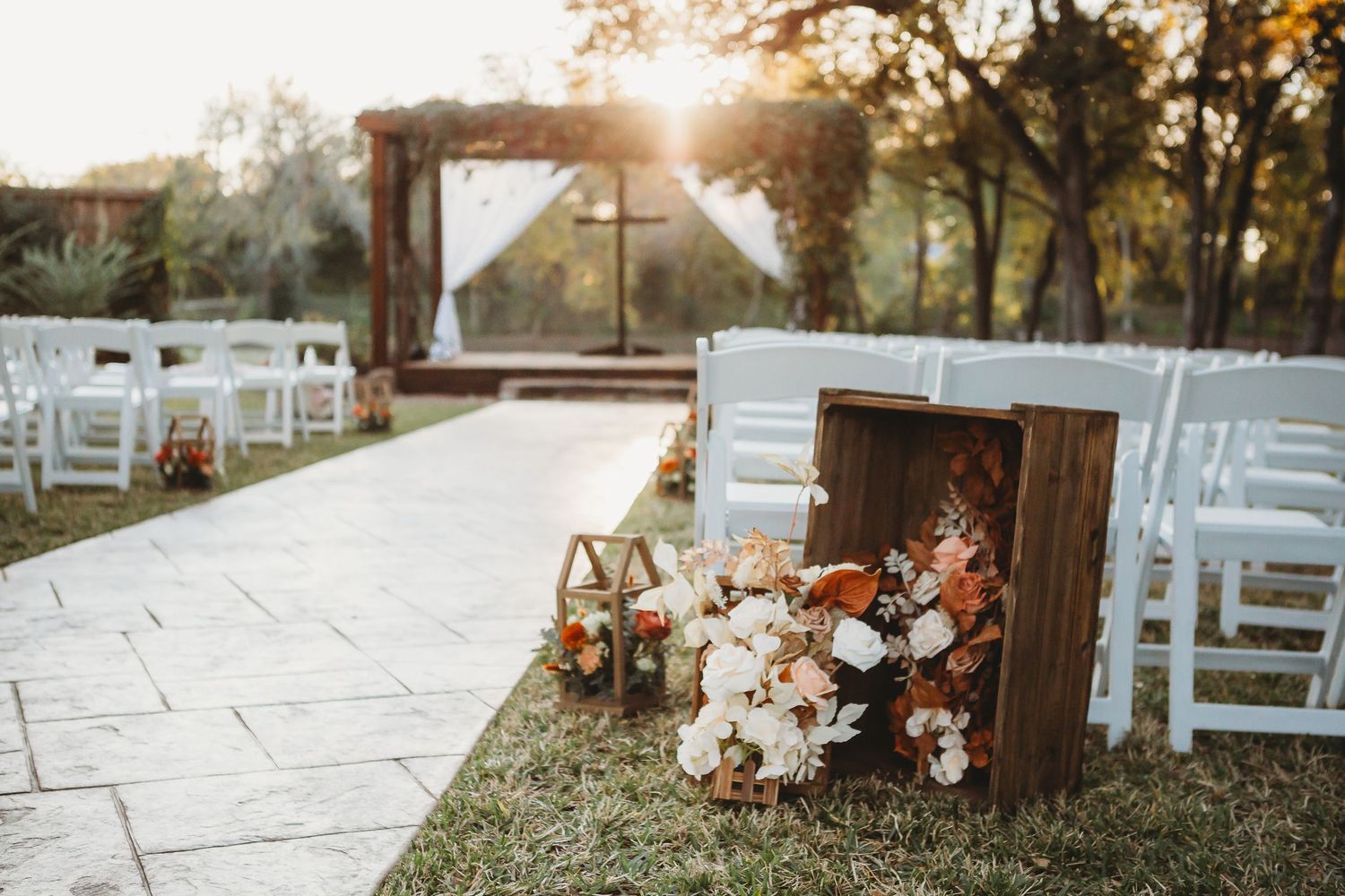 Rustic wooden crates with floral arrangements line outdoor wedding aisle at sunset.