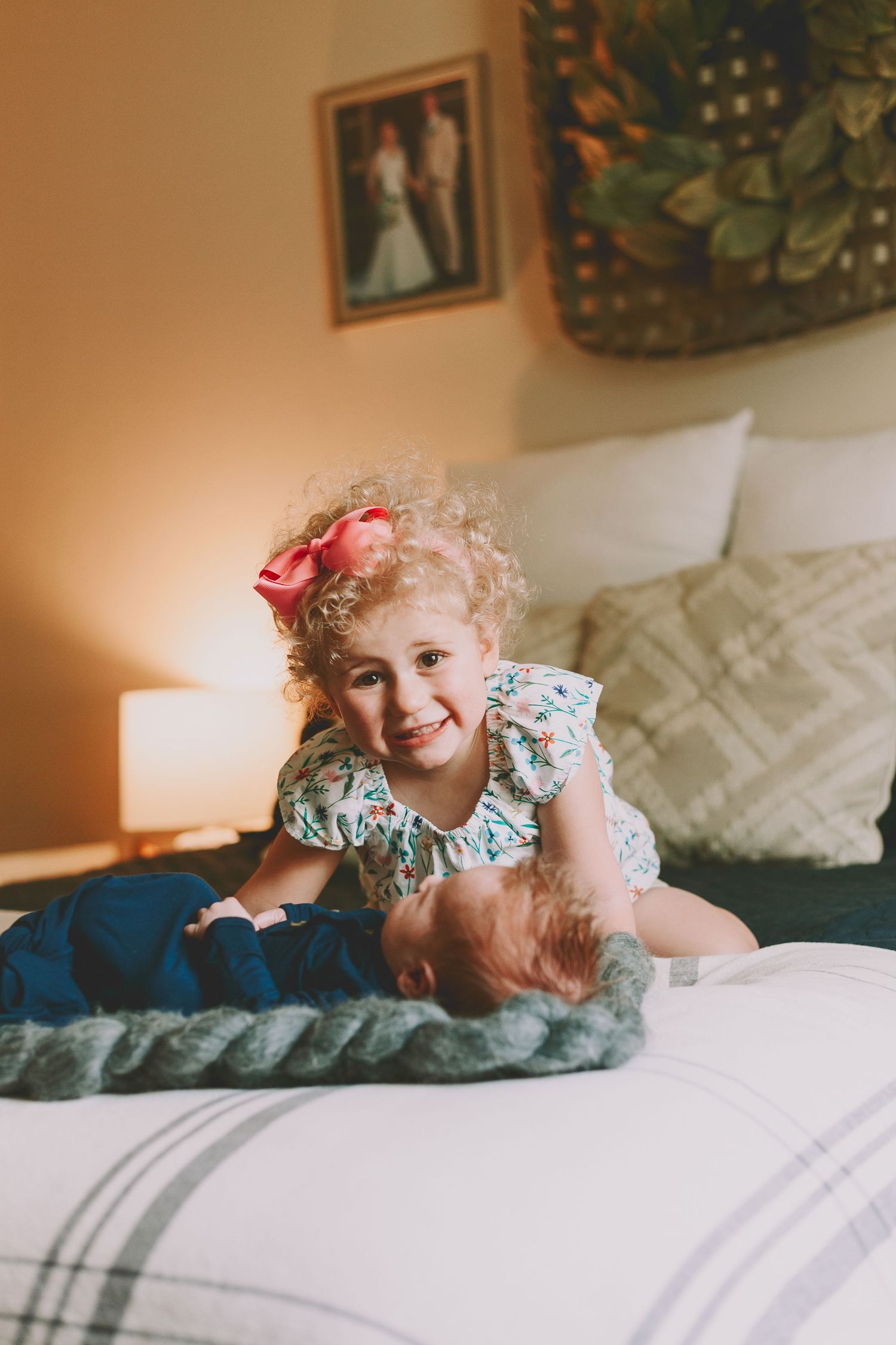 Young child in floral dress playing on a cozy bed with decorative pillows.