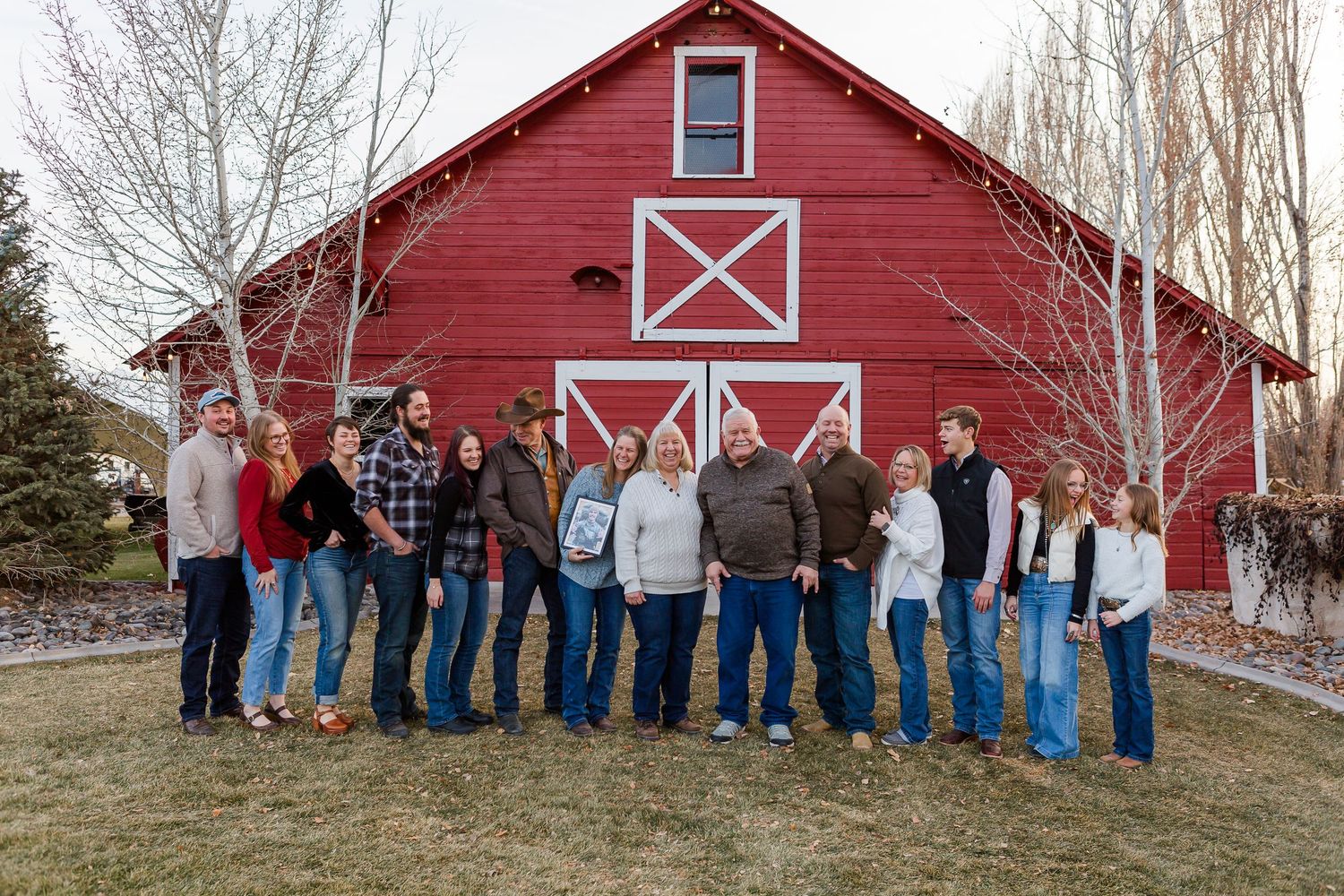 People lined up in front of a classic red barn with decorative white X patterns on a winter day.