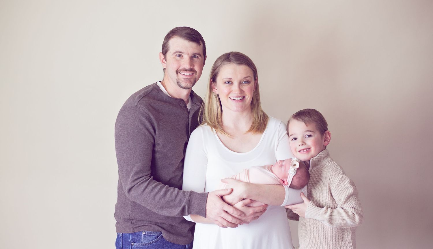 A studio family portrait with a newborn baby in soft, neutral tones.