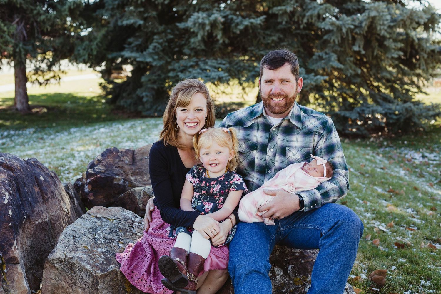 Family seated on large rocks outdoors with evergreen trees in background.