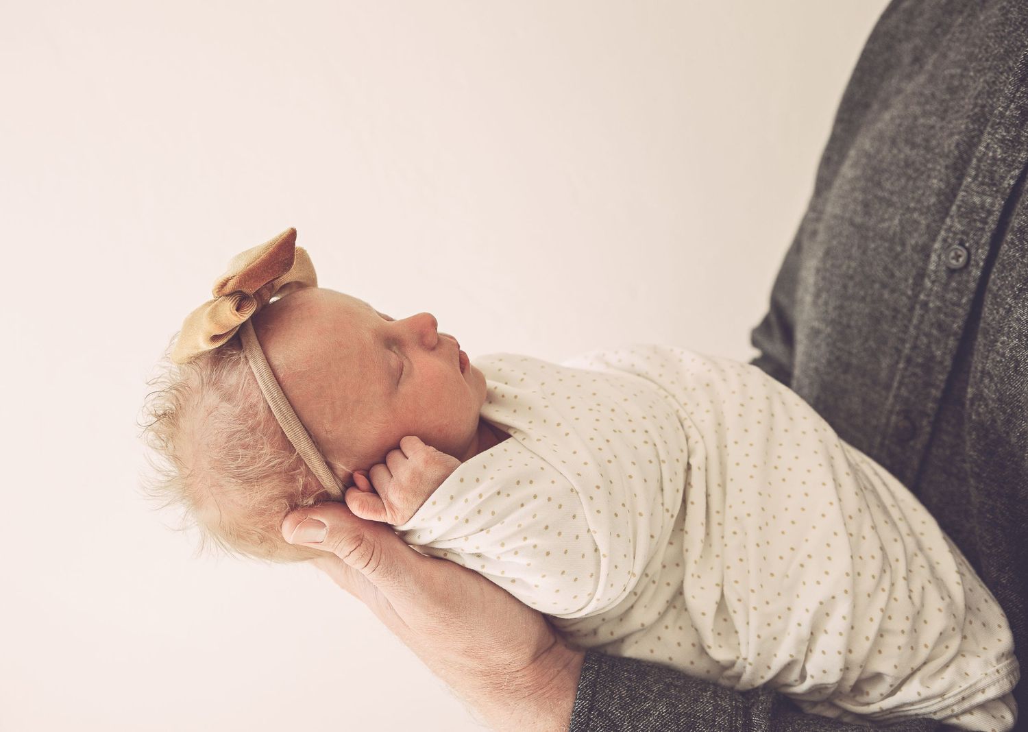 A sleeping baby wrapped in a cream colored swaddle with a small crown accessory rests peacefully.