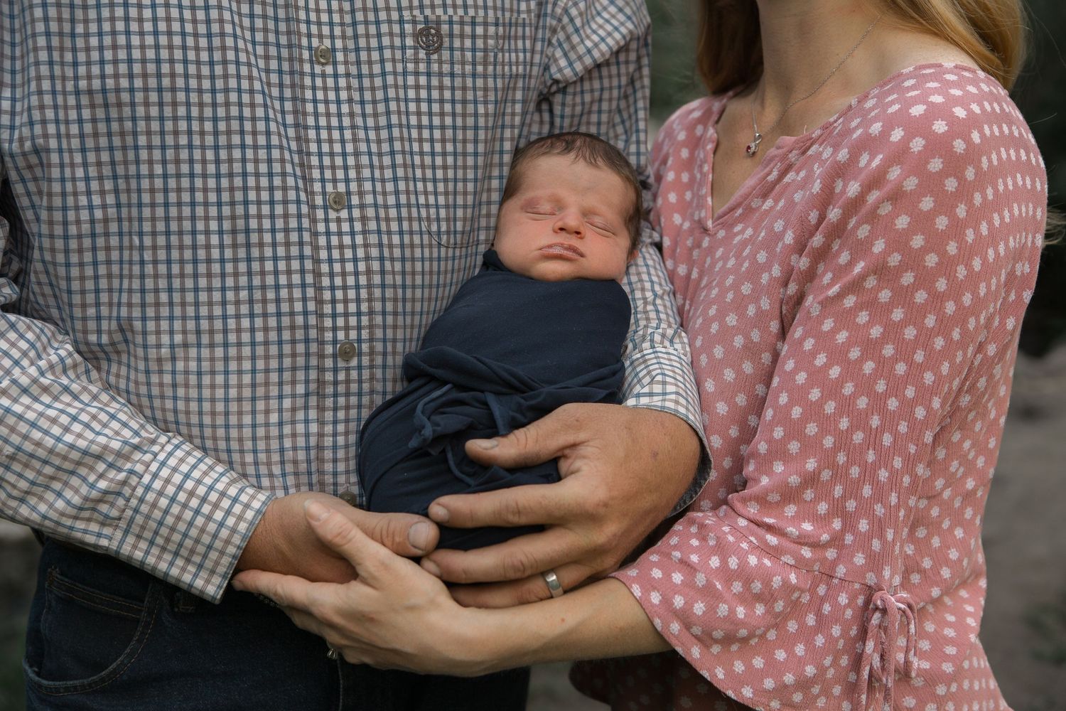 A close-up view of parents cradling their sleeping newborn baby between them.