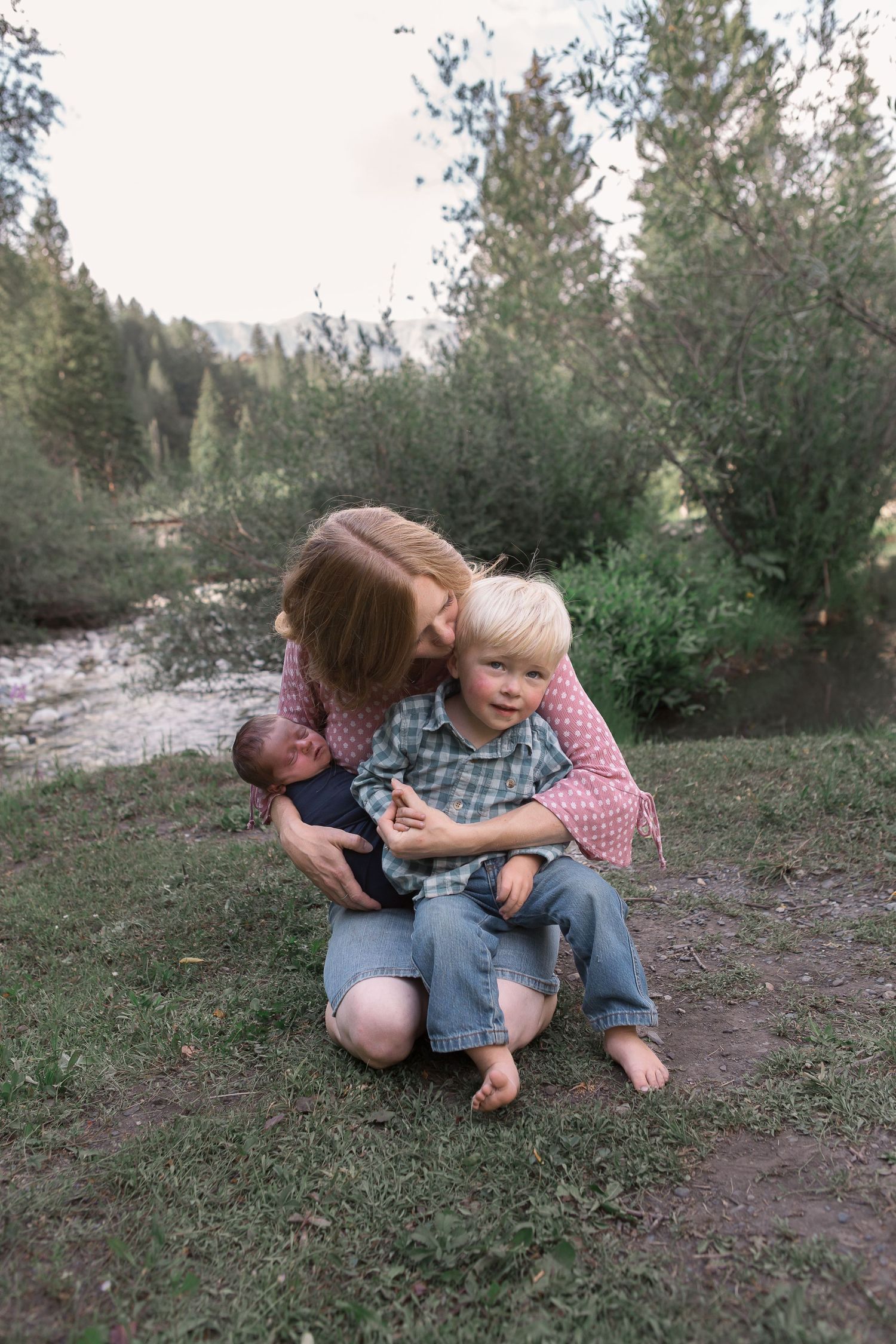 Intimate family moment captured on grassy slope near mountain stream.