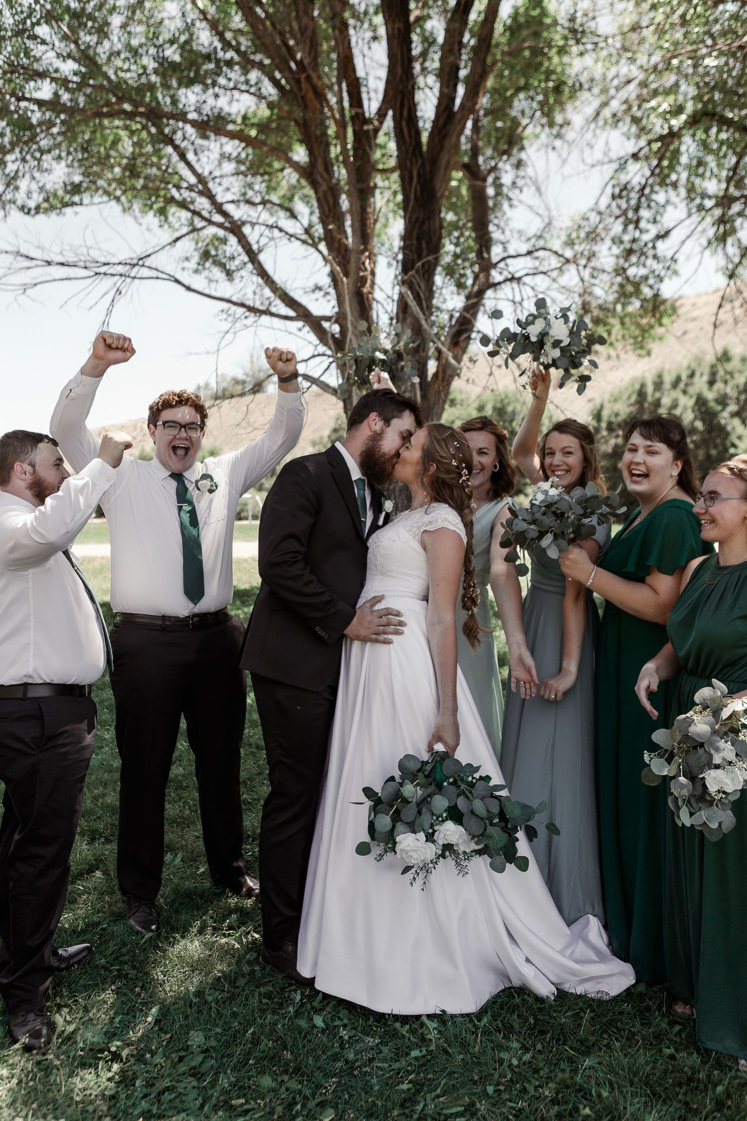 Celebratory moment with wedding party cheering under a tree during outdoor ceremony.