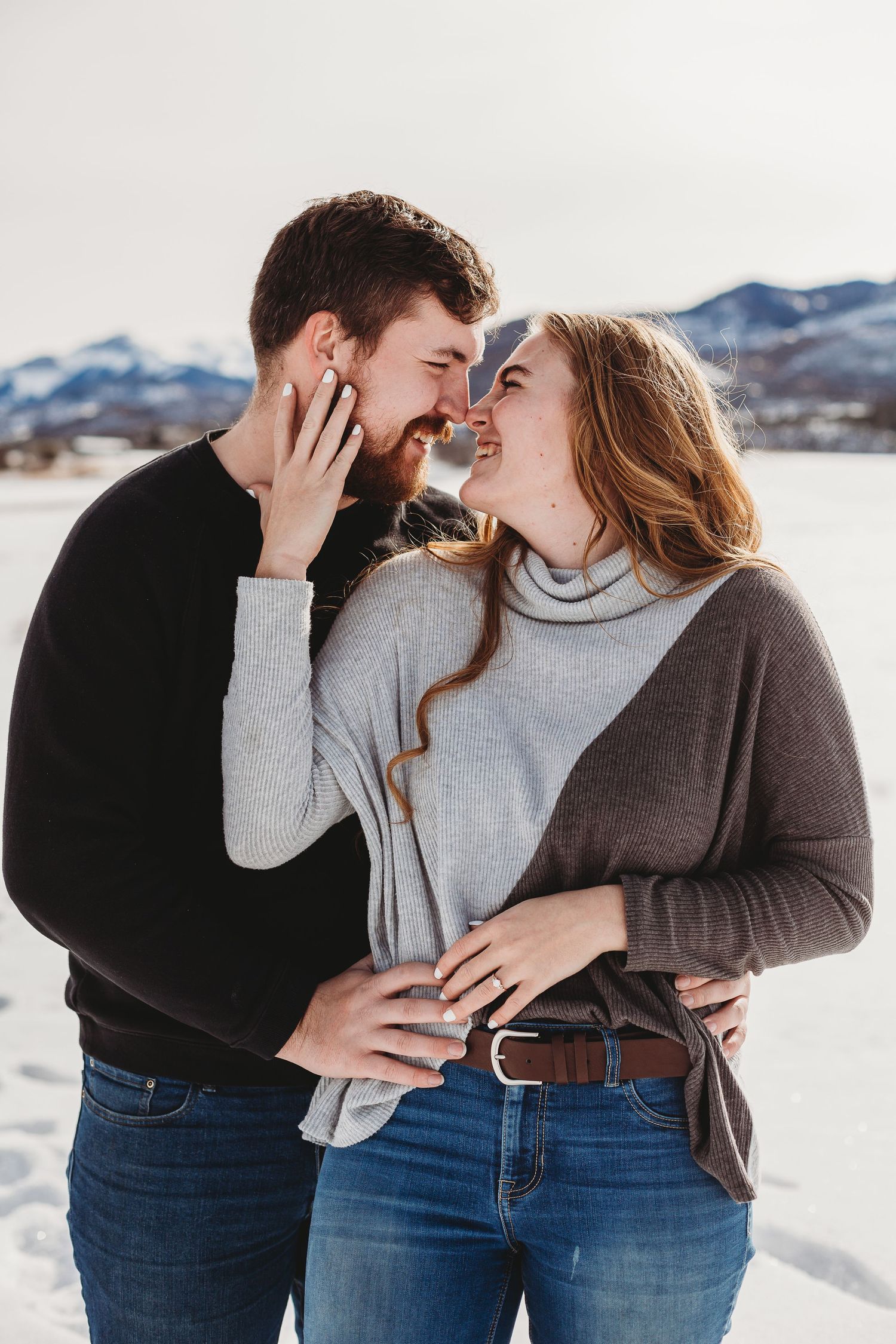 A couple shares an intimate moment while standing in the snow with mountains behind them.