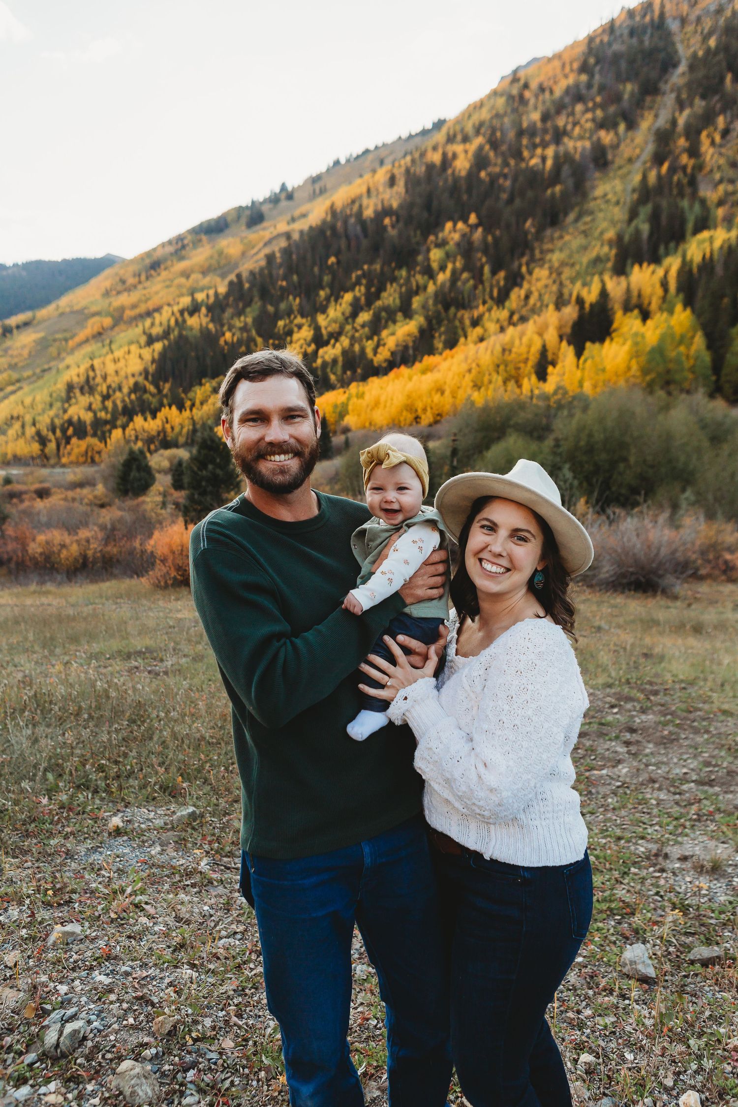 Family stands together in fall colors with mountains and golden aspen trees in background during autumn.